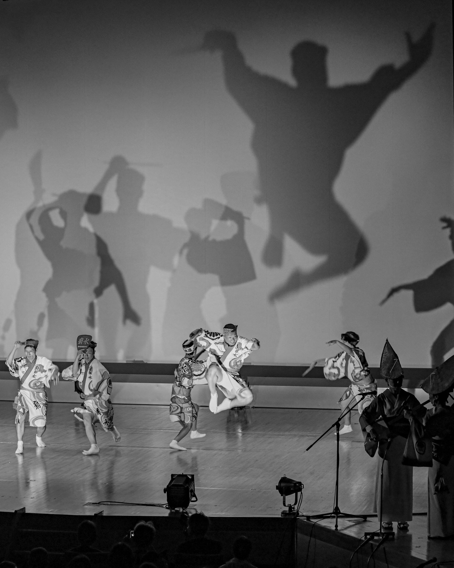 Adegan penari yang tampil di atas panggung dengan bayangan yang diproyeksikan di dinding