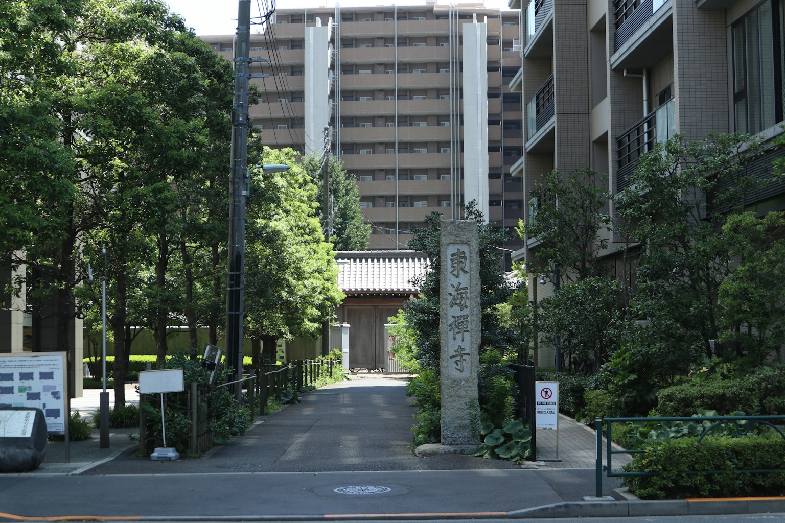 Entrance to a street with an old stone gate surrounded by greenery and a tall building