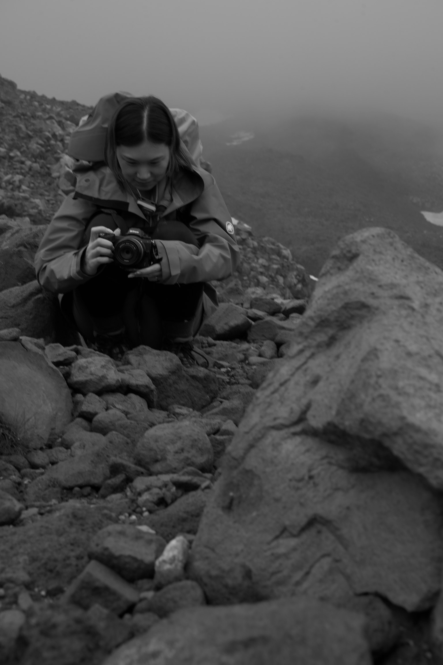 Mujer sentada en rocas en la niebla sosteniendo una cámara