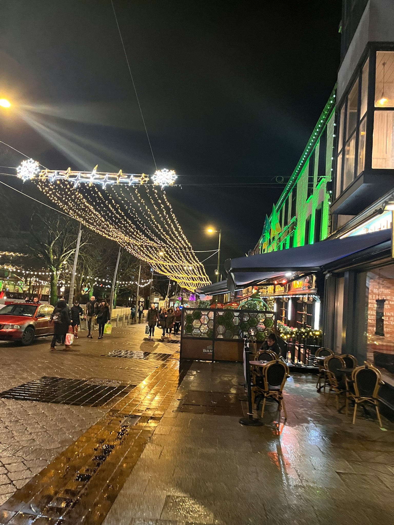 Nächtliche Straßenszene mit beleuchteten Dekorationen und Caféterrasse