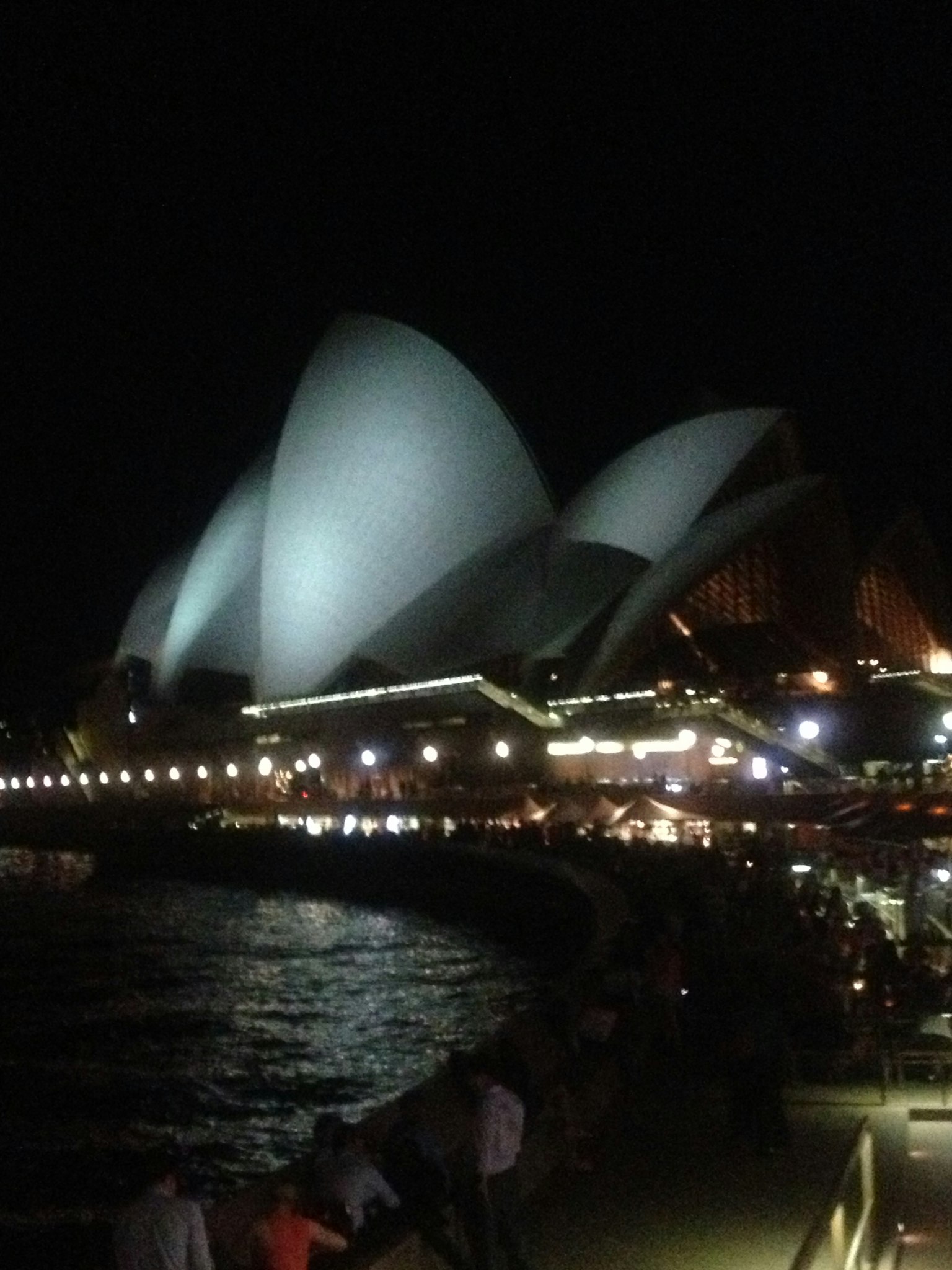 Vista nocturna de la Ópera de Sídney con sus icónicas velas y el puerto