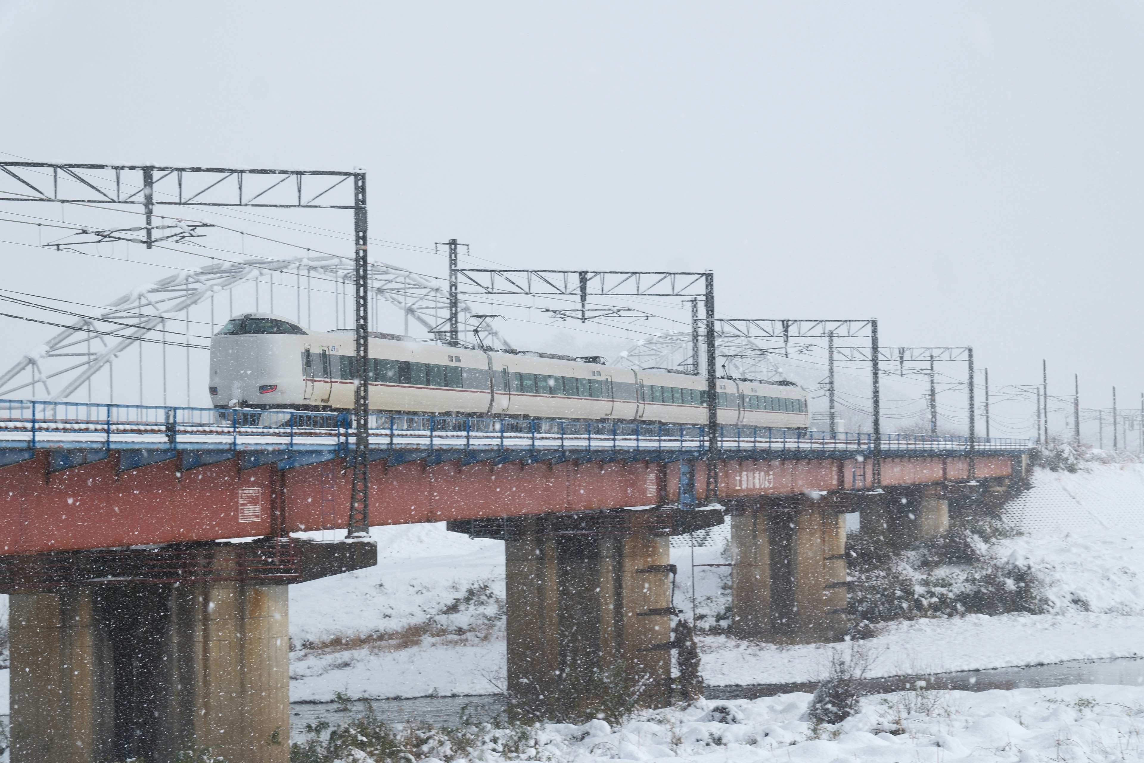 雪の中を走る電車が福知山城近くの橋を渡る風景