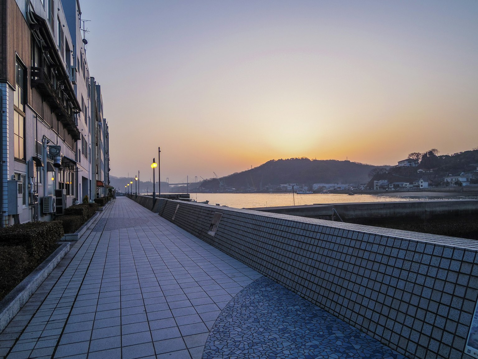 Passeggiata tranquilla lungo il fiume con edifici e tramonto sullo sfondo