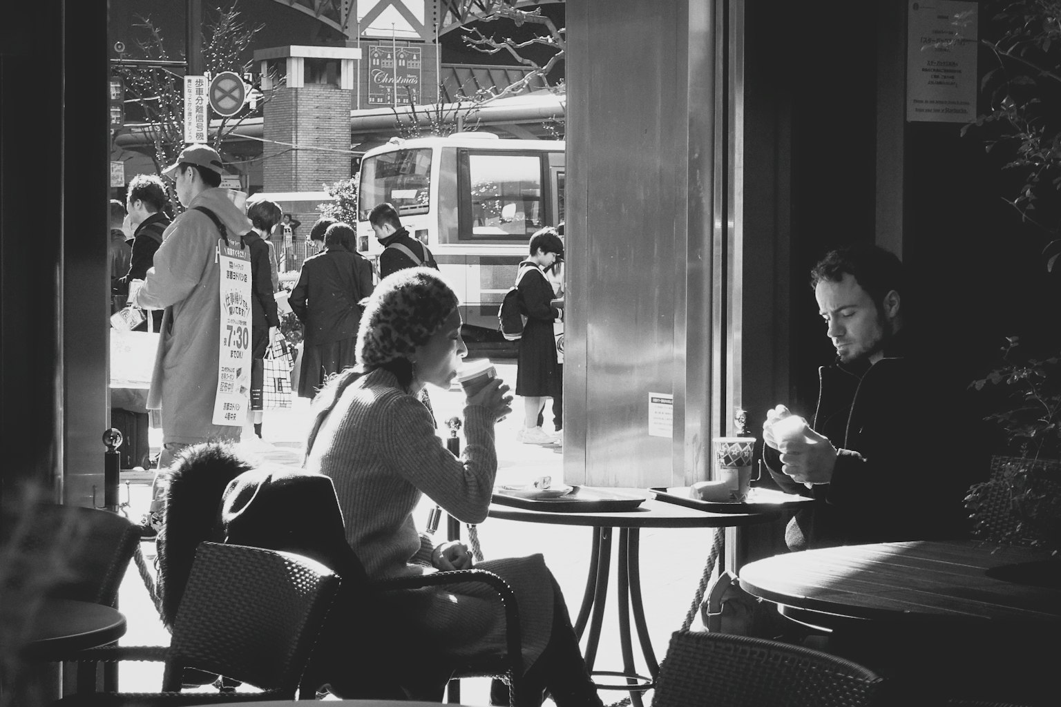 Foto hitam putih dua orang di kafe menikmati minuman dengan pejalan kaki di luar
