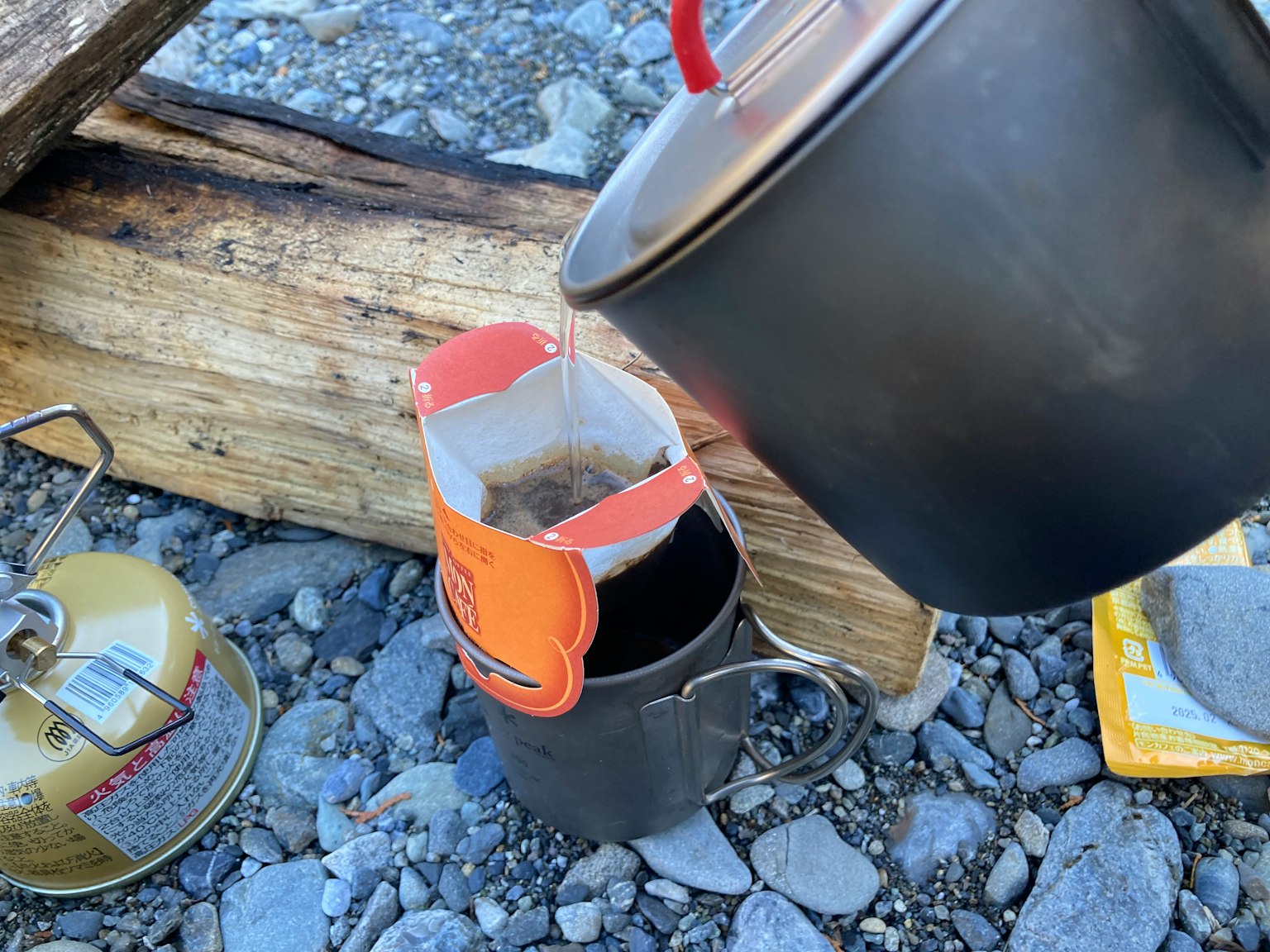 Outdoor coffee brewing scene featuring a steel coffee pot and cup