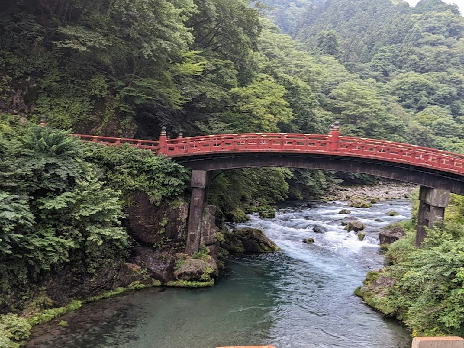 ทิวทัศน์ที่สวยงามของสะพานสีแดงข้ามแม่น้ำที่ไหลผ่าน surrounded by greenery