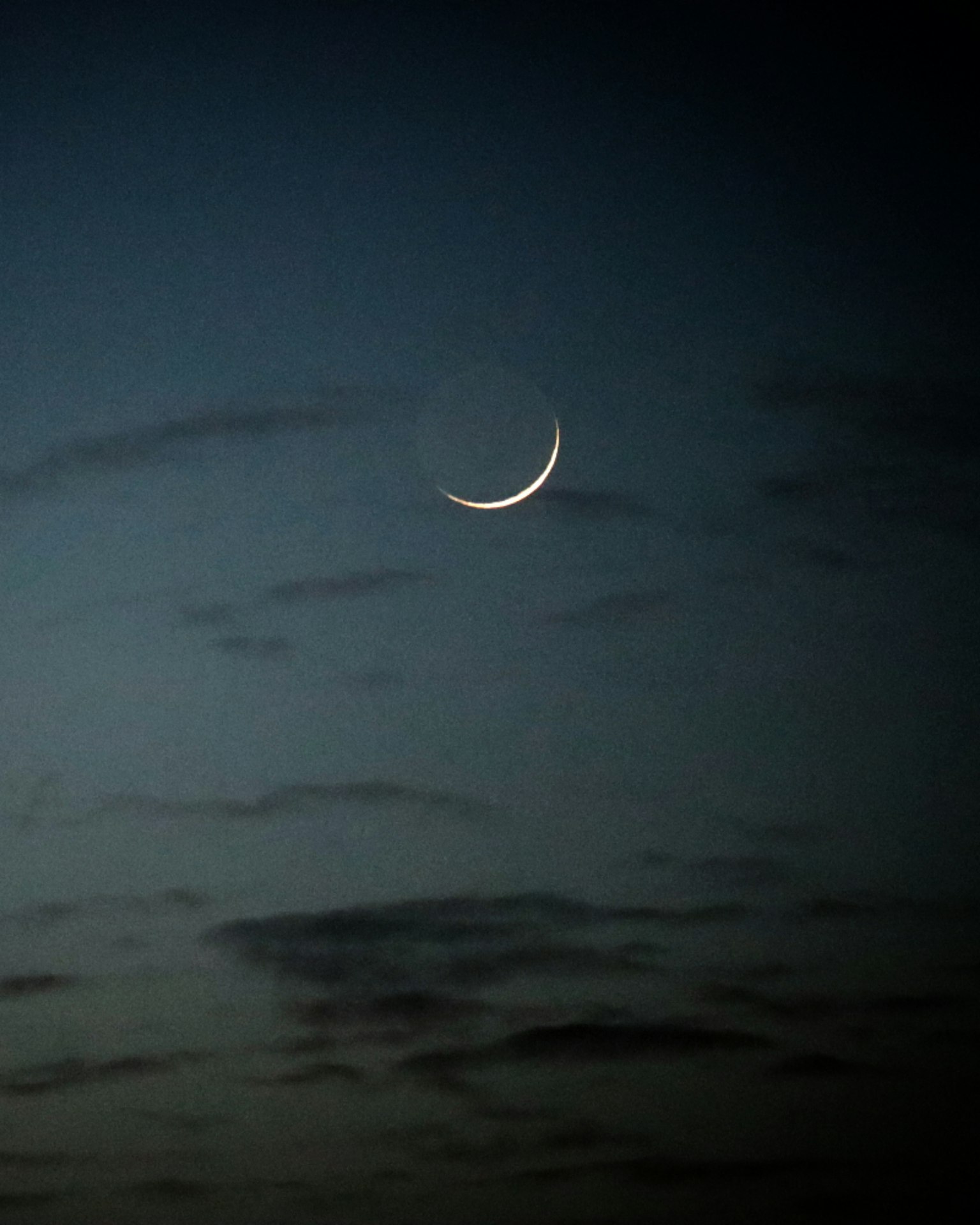 Dünne Mondsichel in einem Dämmerungshimmel mit Wolken