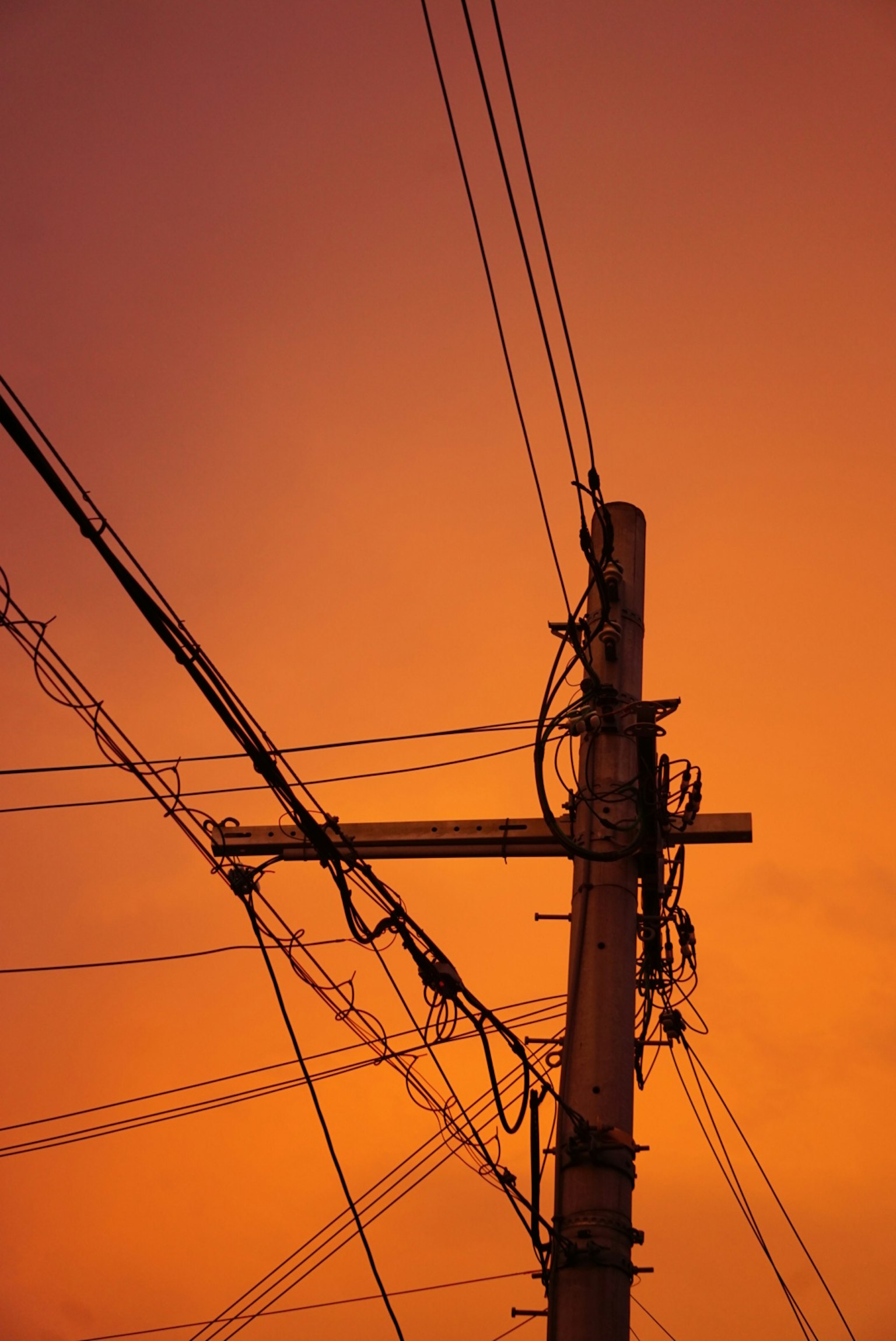 Strommast silhouettiert vor einem orangefarbenen Sonnenuntergangshimmel