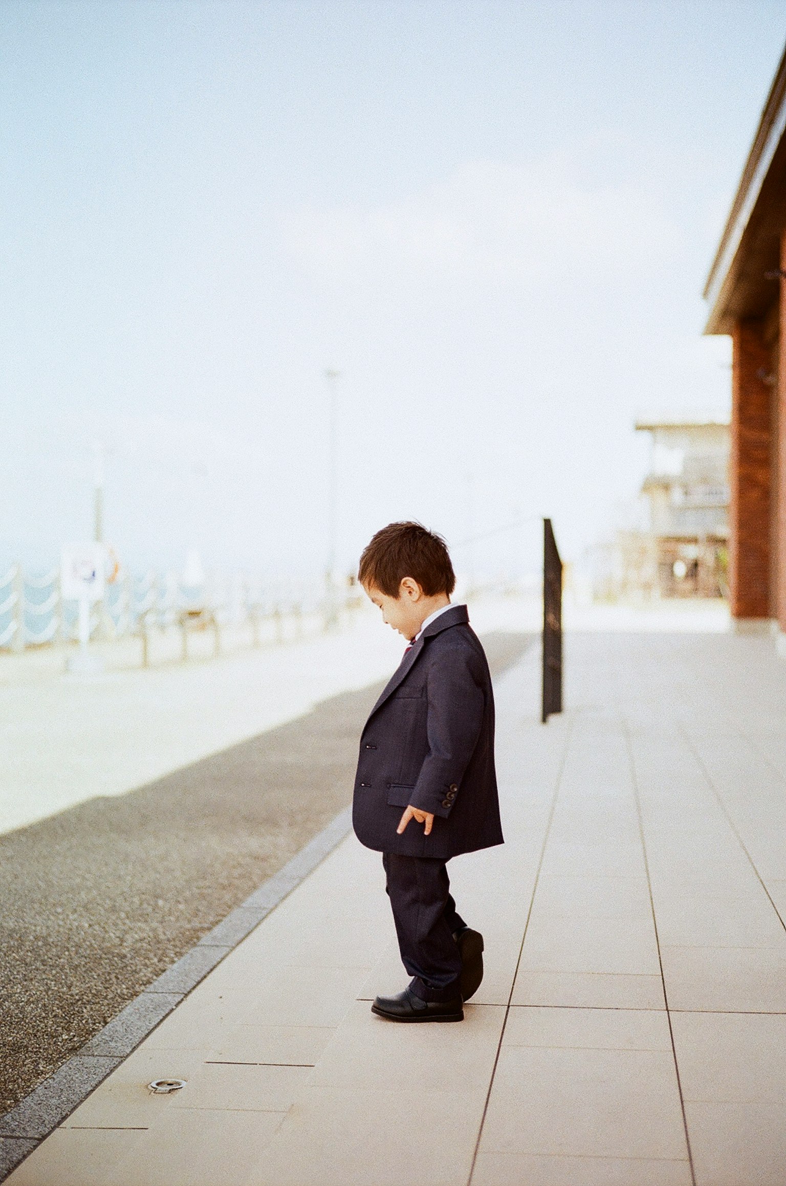 A child in a suit standing on a sidewalk looking down