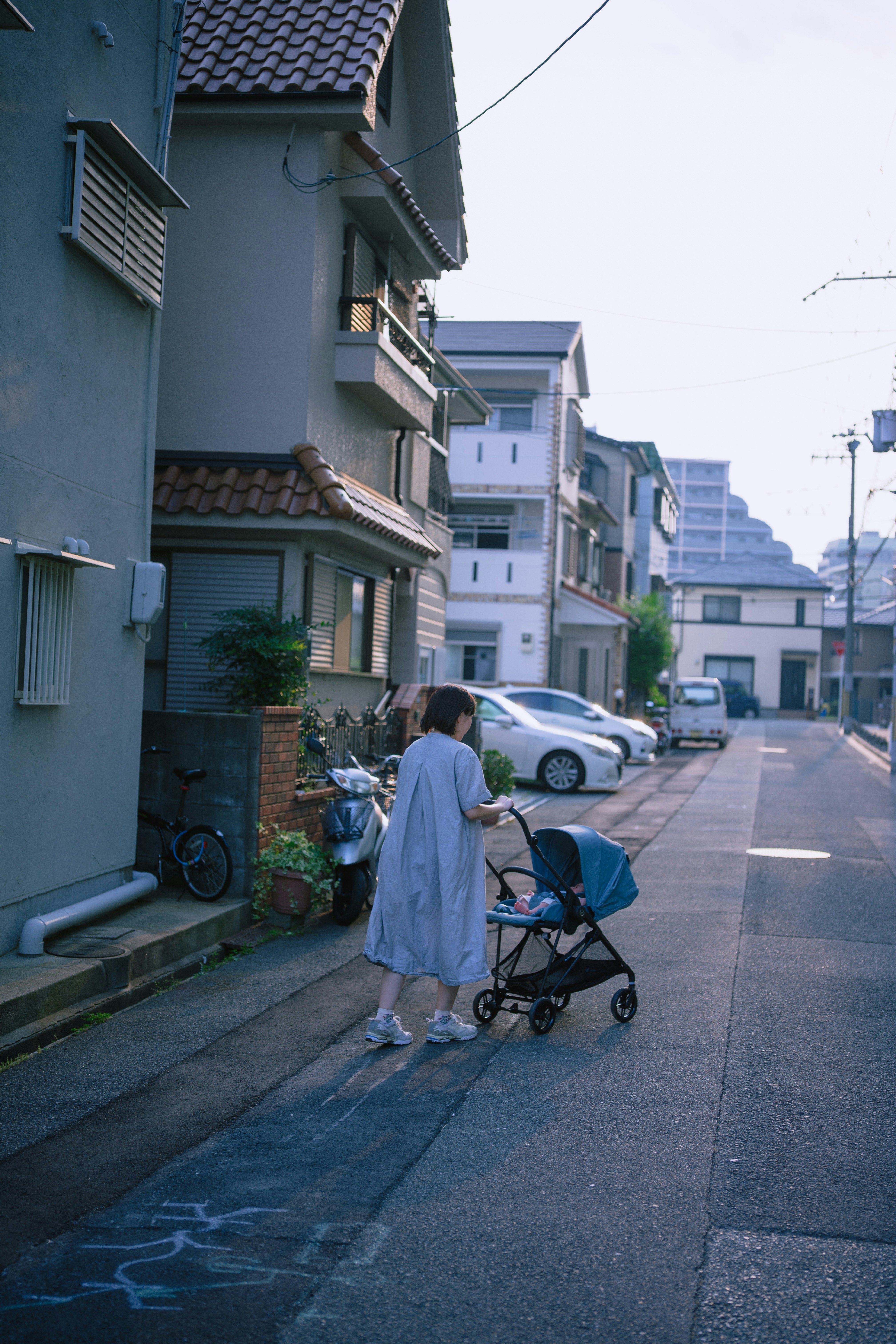 路地でベビーカーを押す人のある住宅街の風景