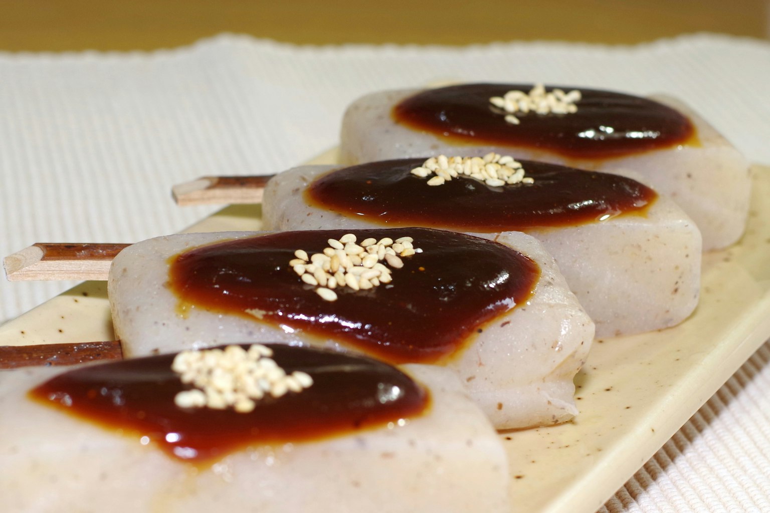 Pasteles de arroz blancos cubiertos con salsa dulce y semillas de sésamo en un plato de madera