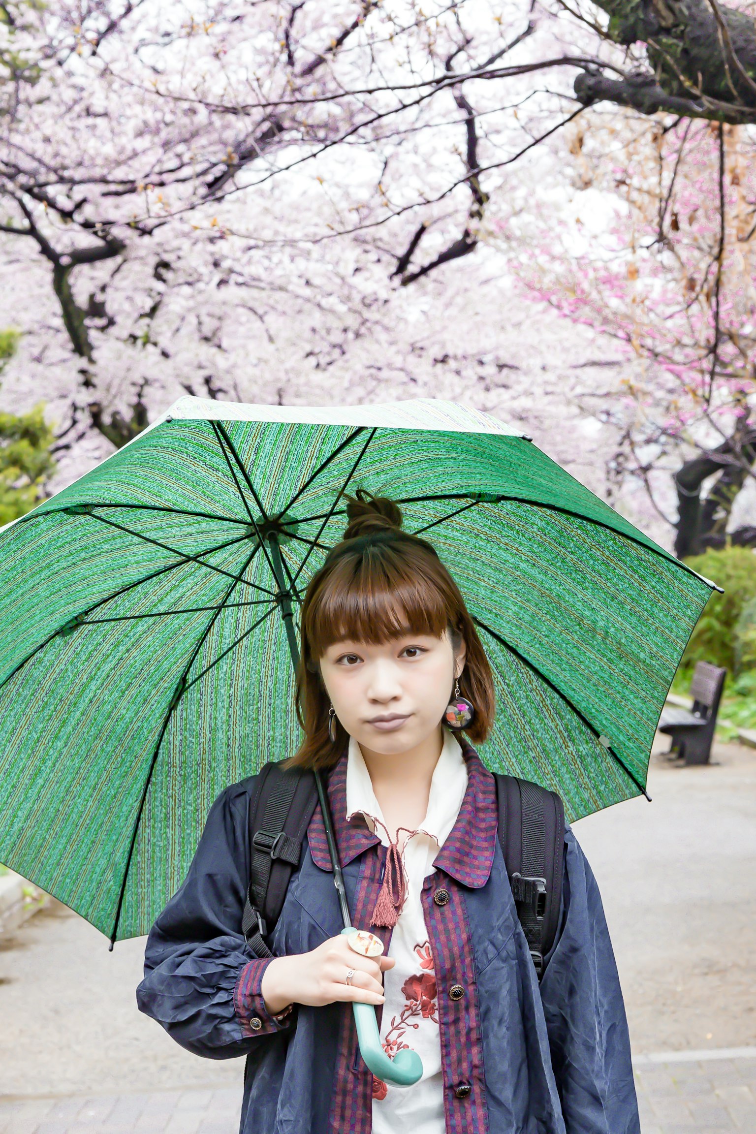 Girl holding a green umbrella under cherry blossom trees