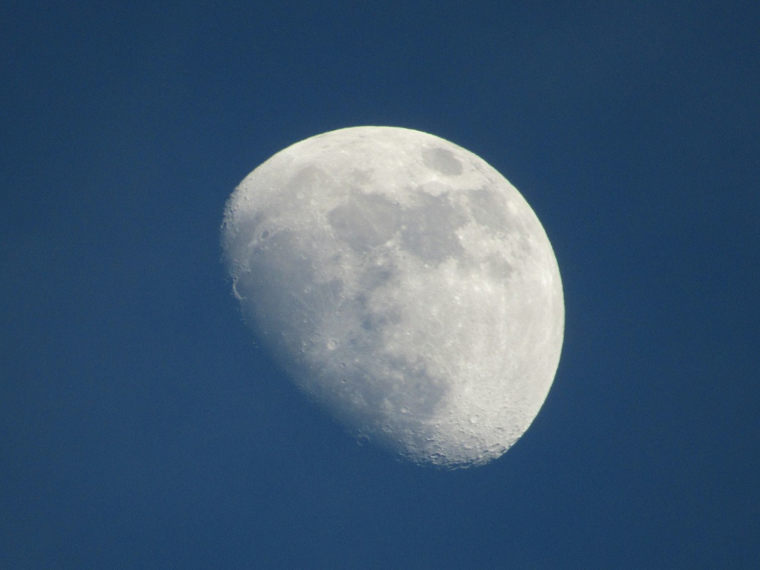Bulan sabit dengan kawah terlihat di latar belakang langit biru