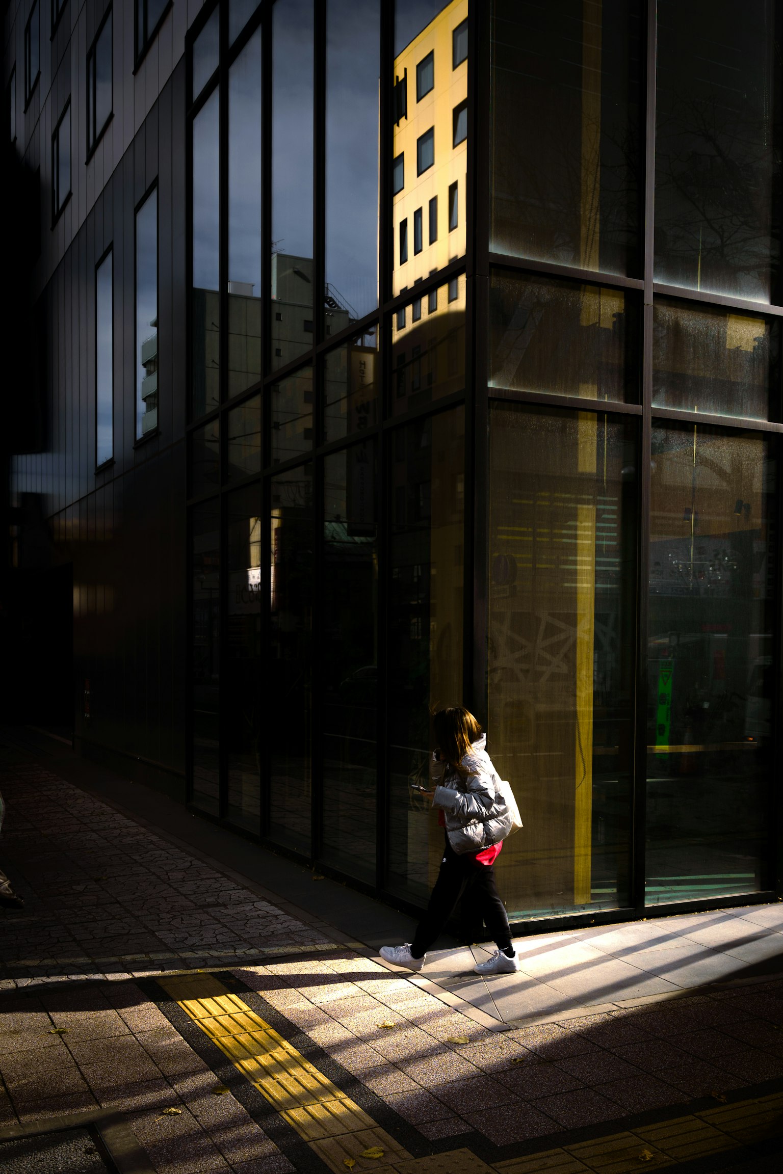 Silhouette d'une femme marchant devant un bâtiment en verre avec des ombres contrastées