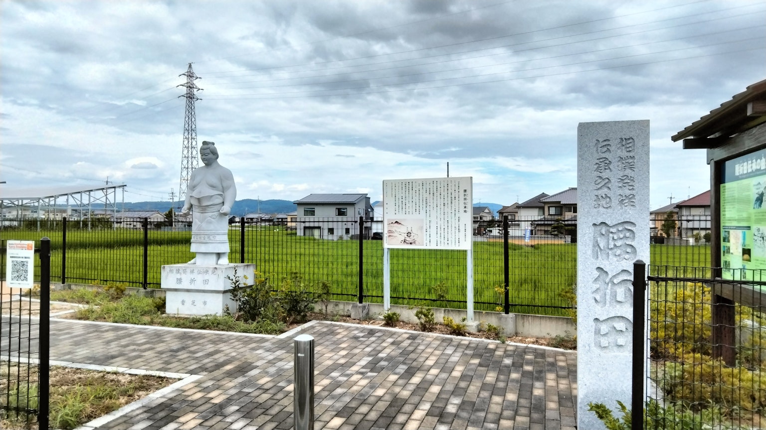 Landscape featuring a white statue near rice fields and informational signs
