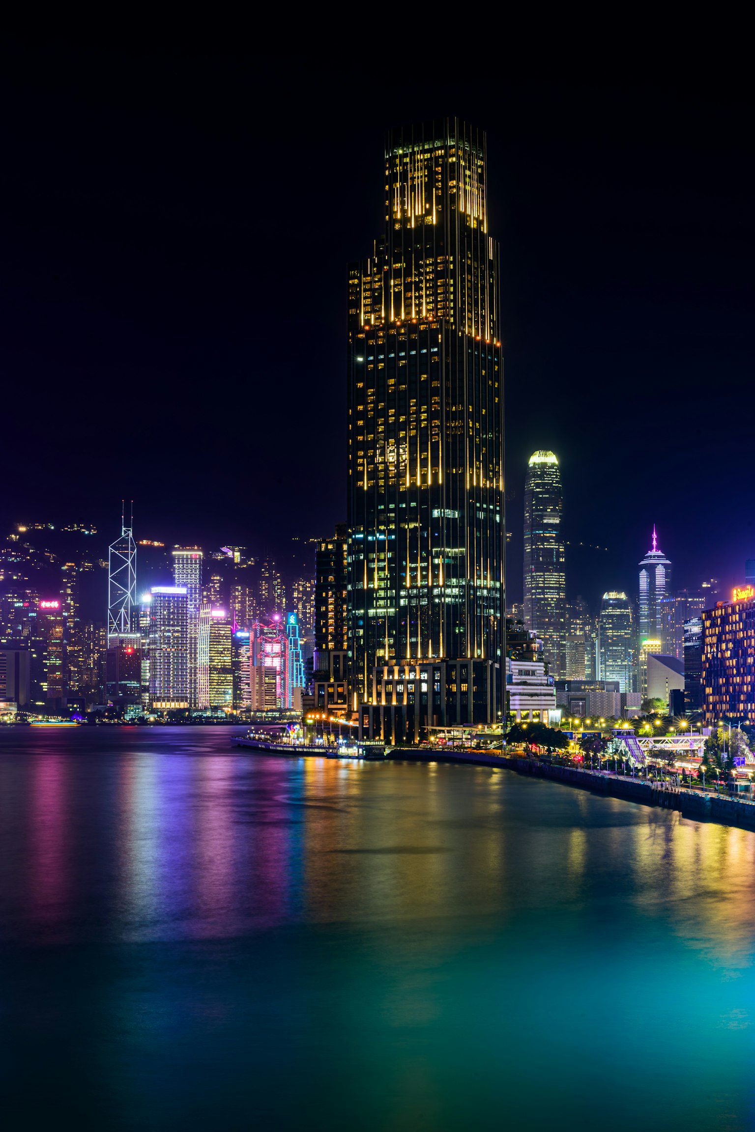 Vista nocturna del horizonte de Hong Kong con rascacielos iluminados y reflejos coloridos en el agua