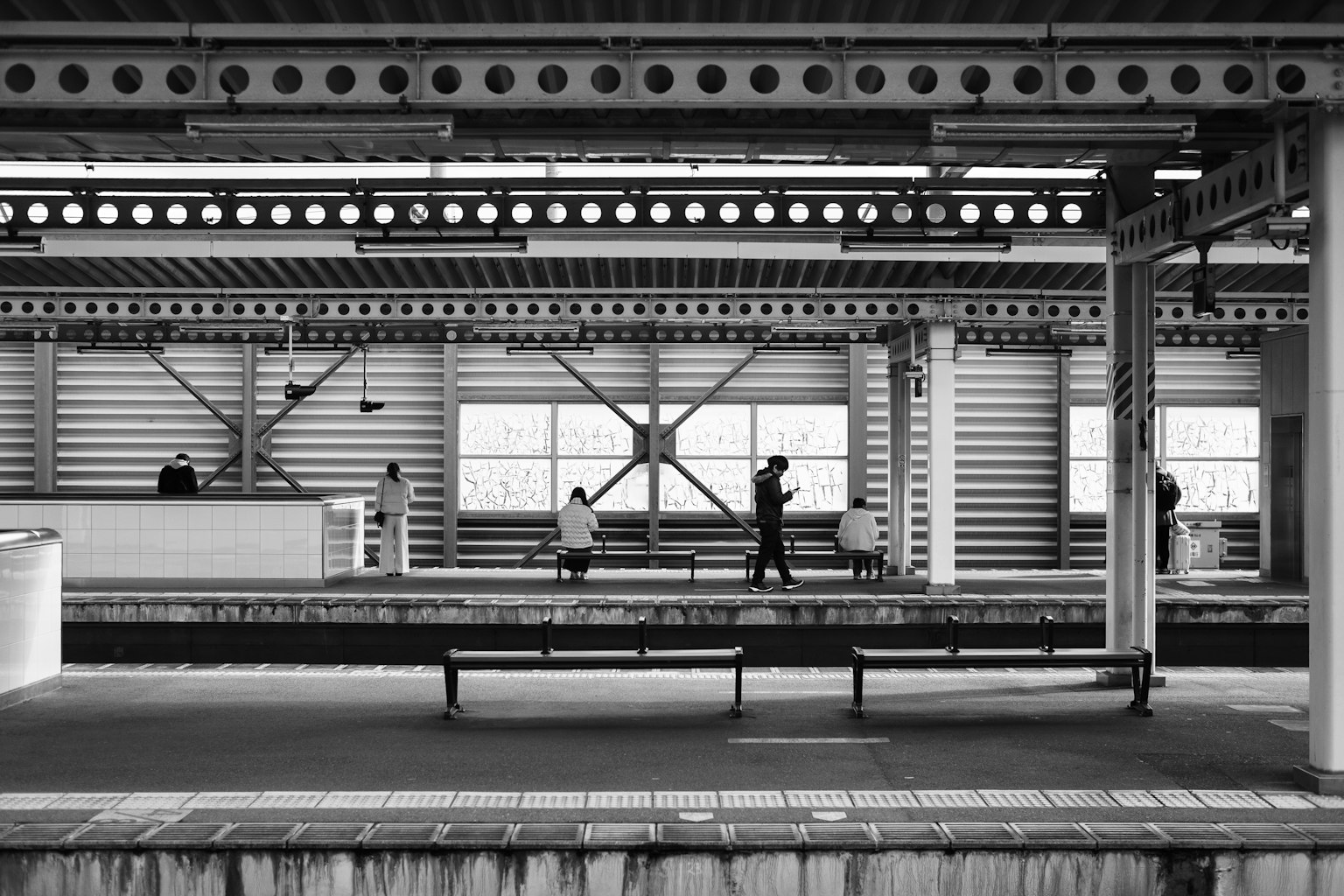 Image en noir et blanc d'une plateforme de gare avec des personnes et des bancs