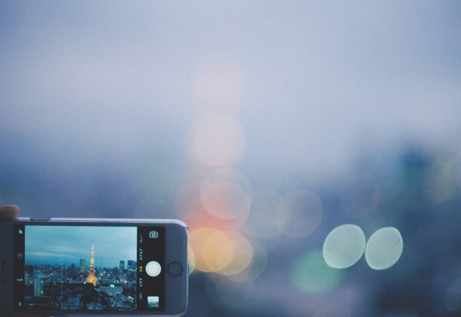 Ein Smartphone, das den Tokyo Tower mit einer verschwommenen Stadtlandschaft im Hintergrund aufnimmt