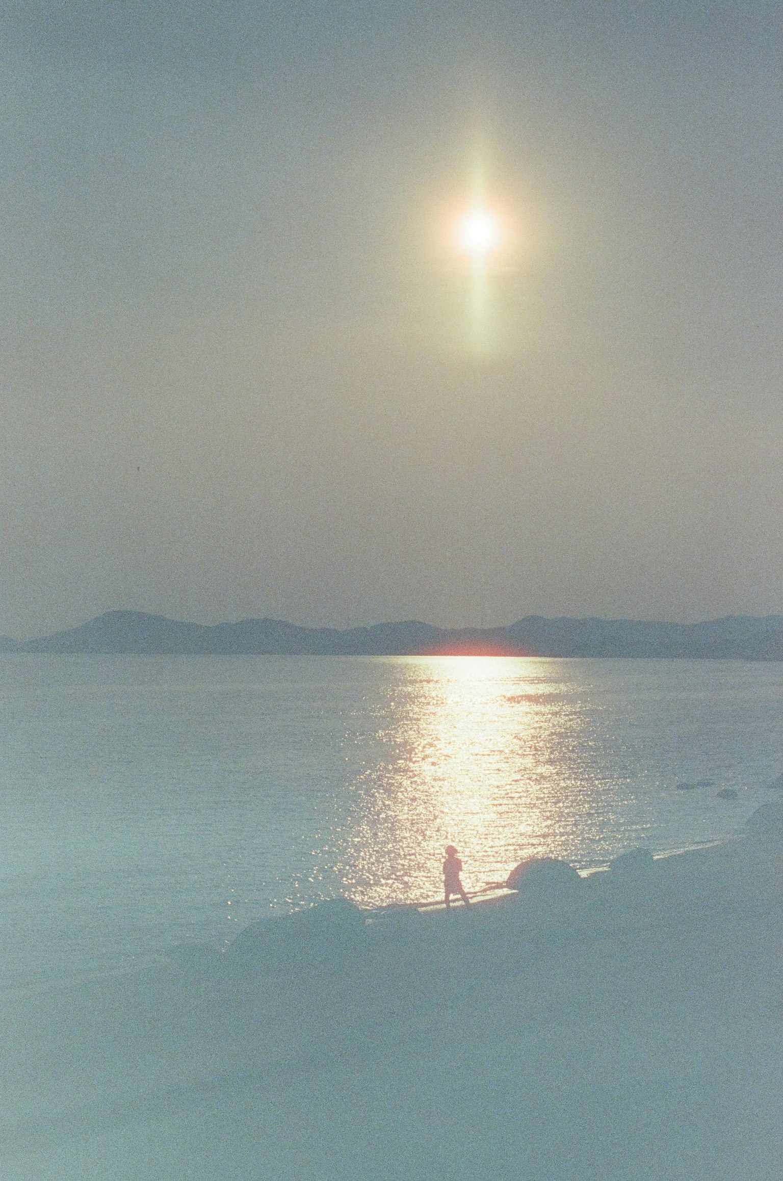 Silhouette d'une personne se tenant près d'une mer calme reflétant le coucher de soleil