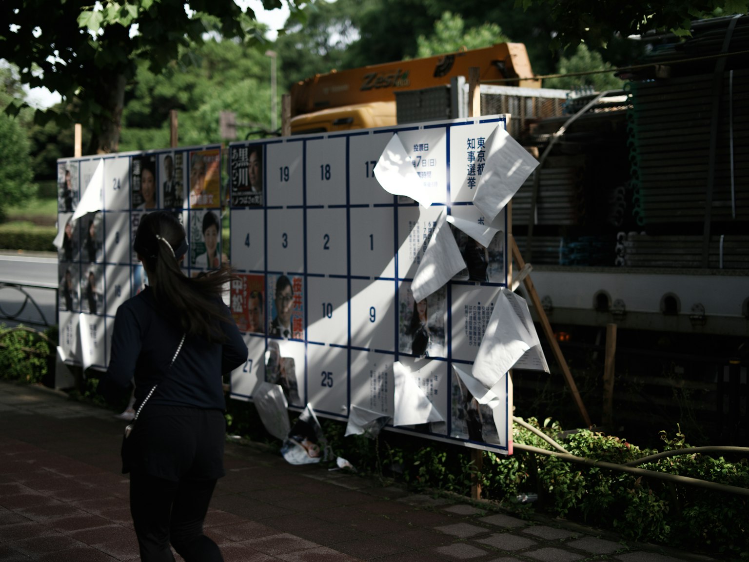 Une personne marchant devant un mur de posters flottants au soleil