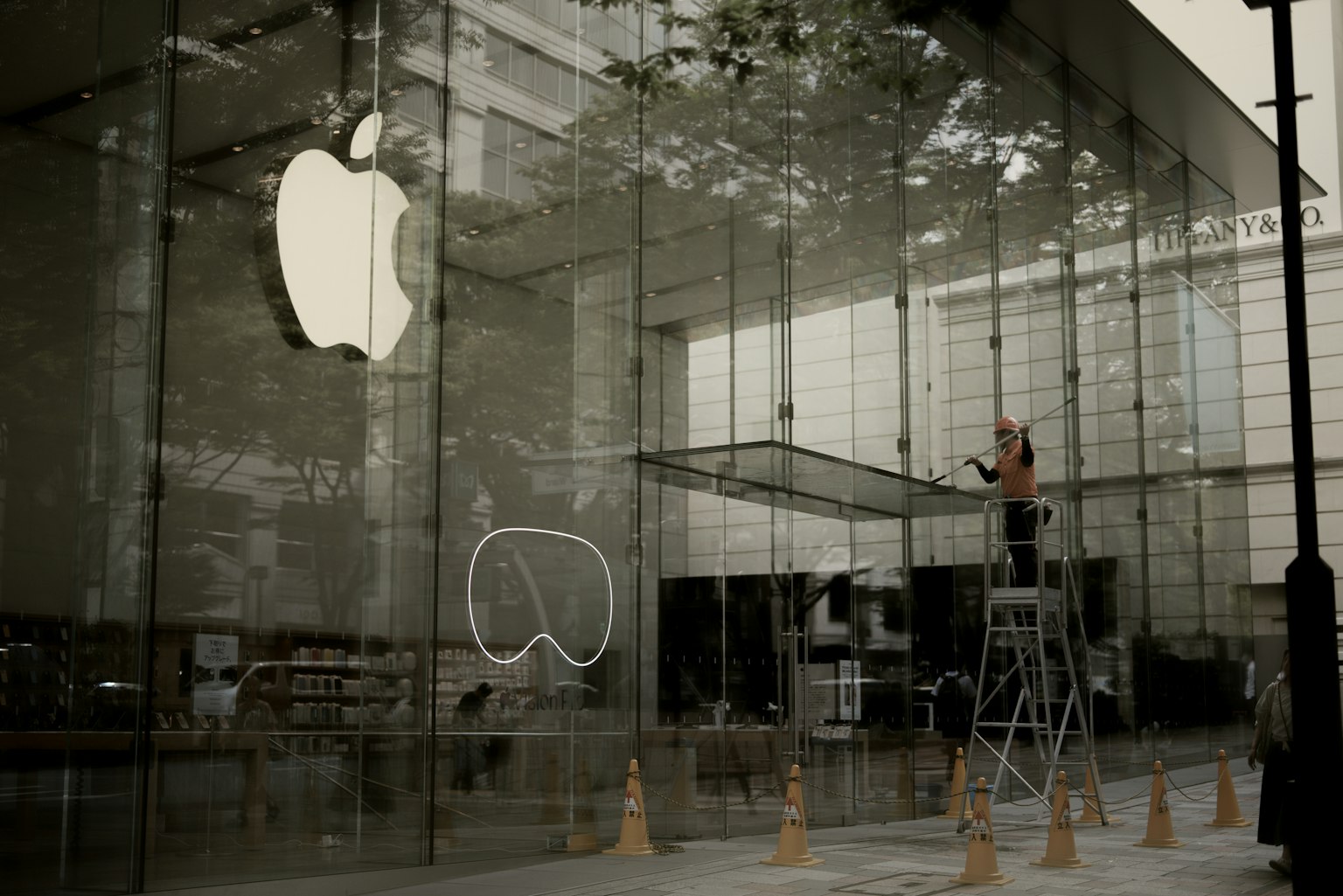 Person cleaning the glass front of an Apple Store with the iconic logo visible