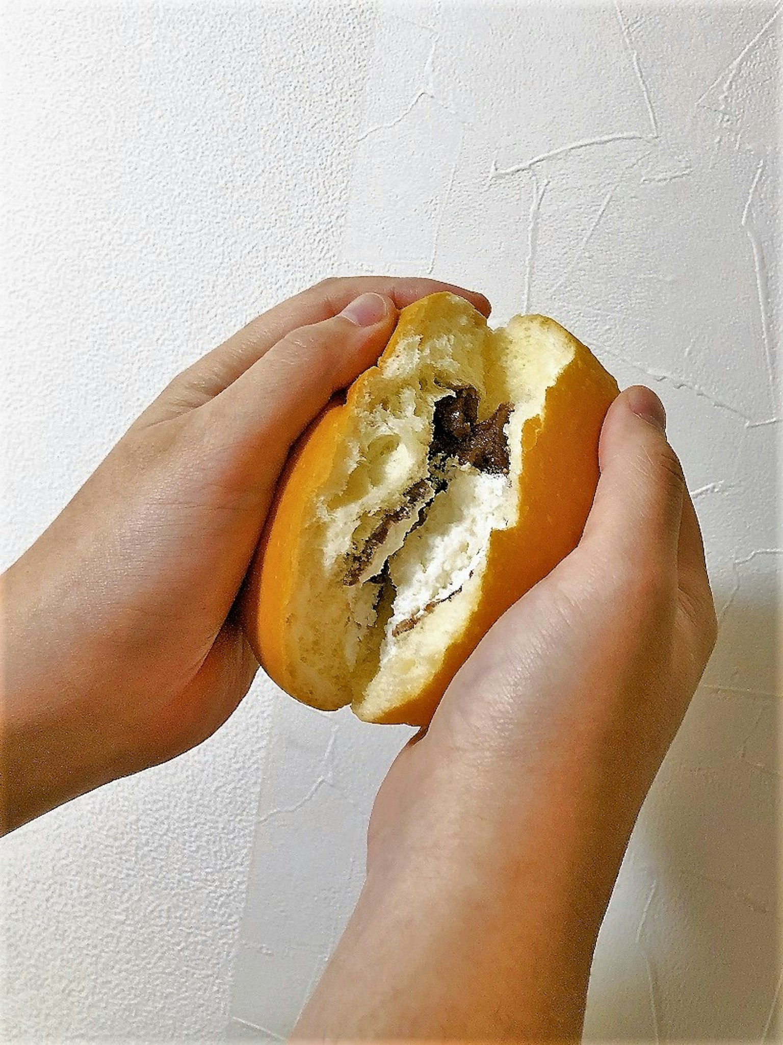 Un panino ripieno di crema spezzato a metà, tenuto in mano