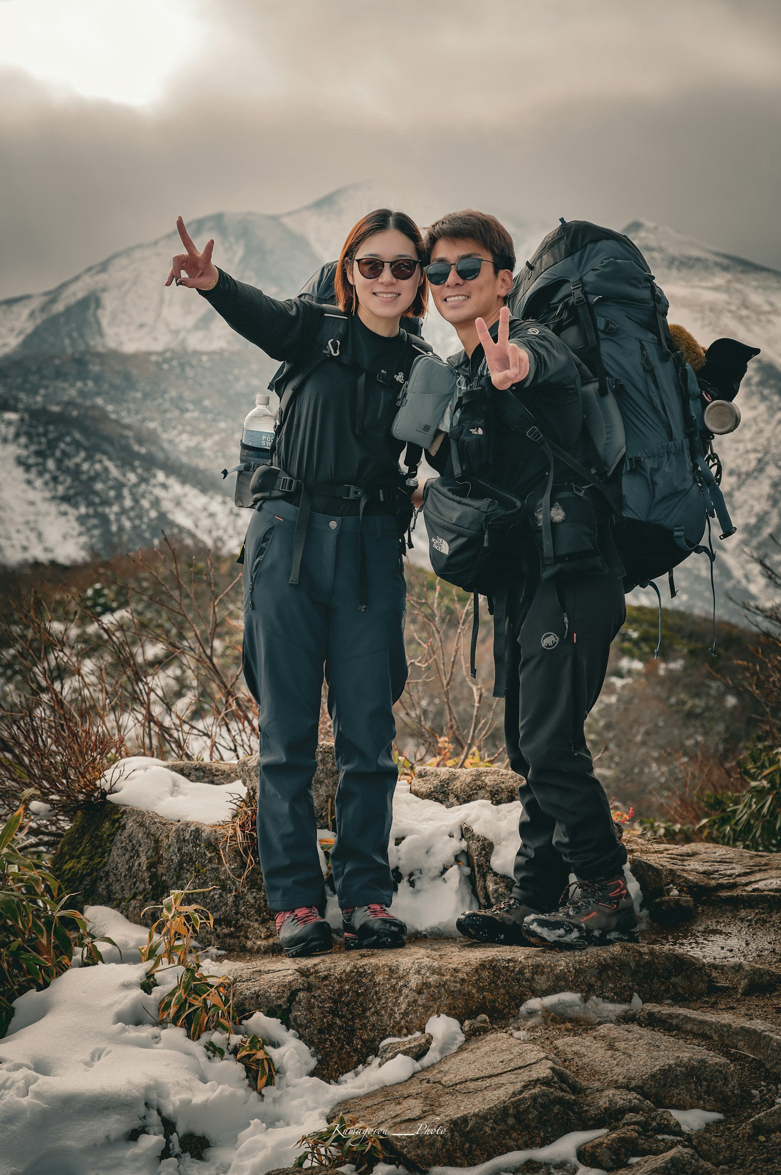Due escursionisti in posa sulla cima della montagna con picchi innevati sullo sfondo