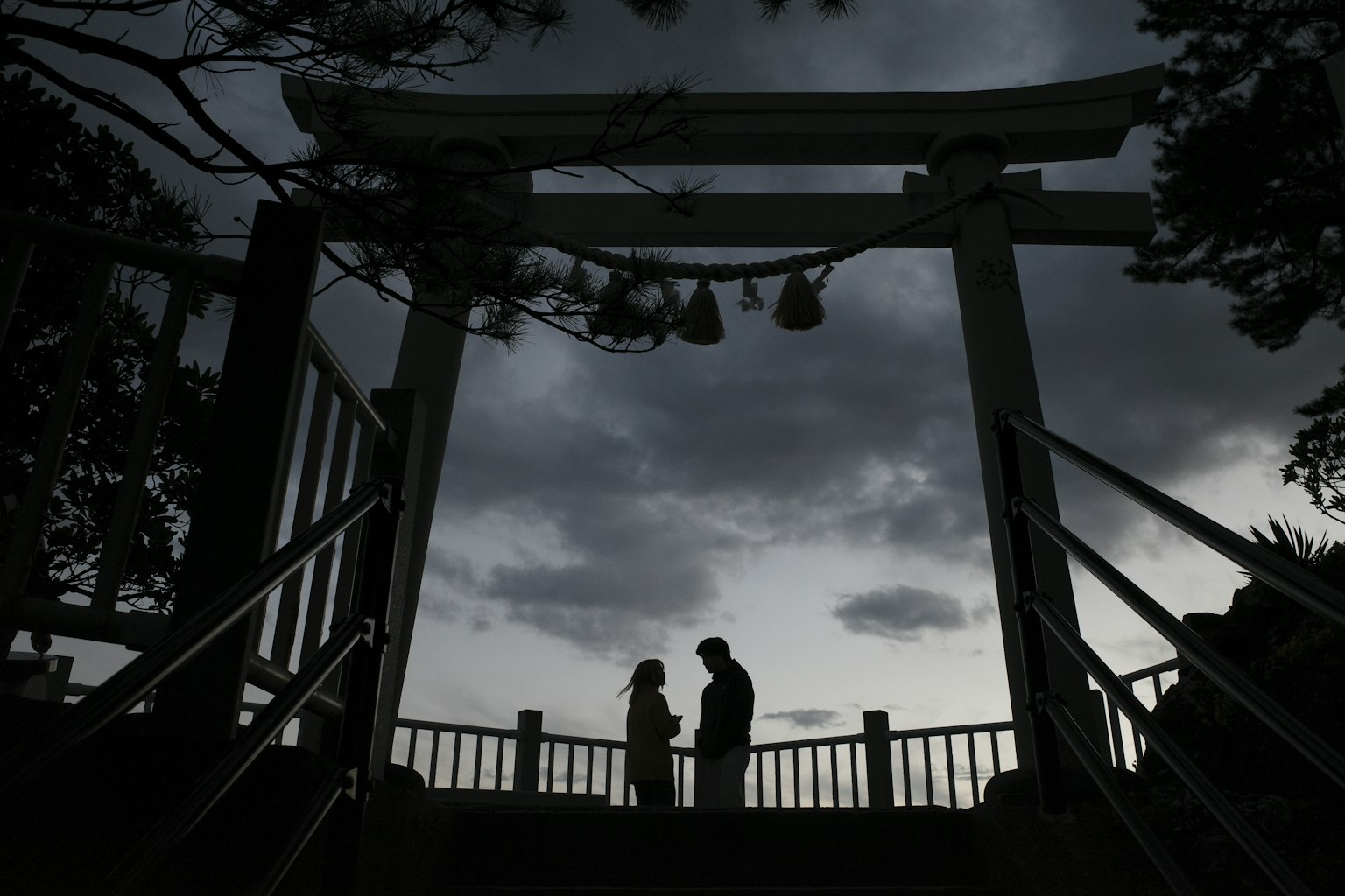 Silhouette of a couple standing in front of a torii gate under a dark sky