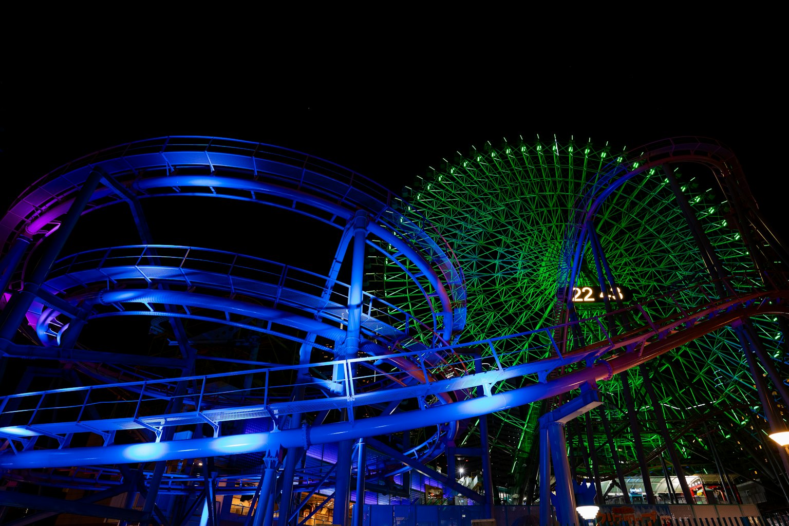 Rueda de la fortuna y montaña rusa iluminadas por la noche con luces azules y verdes