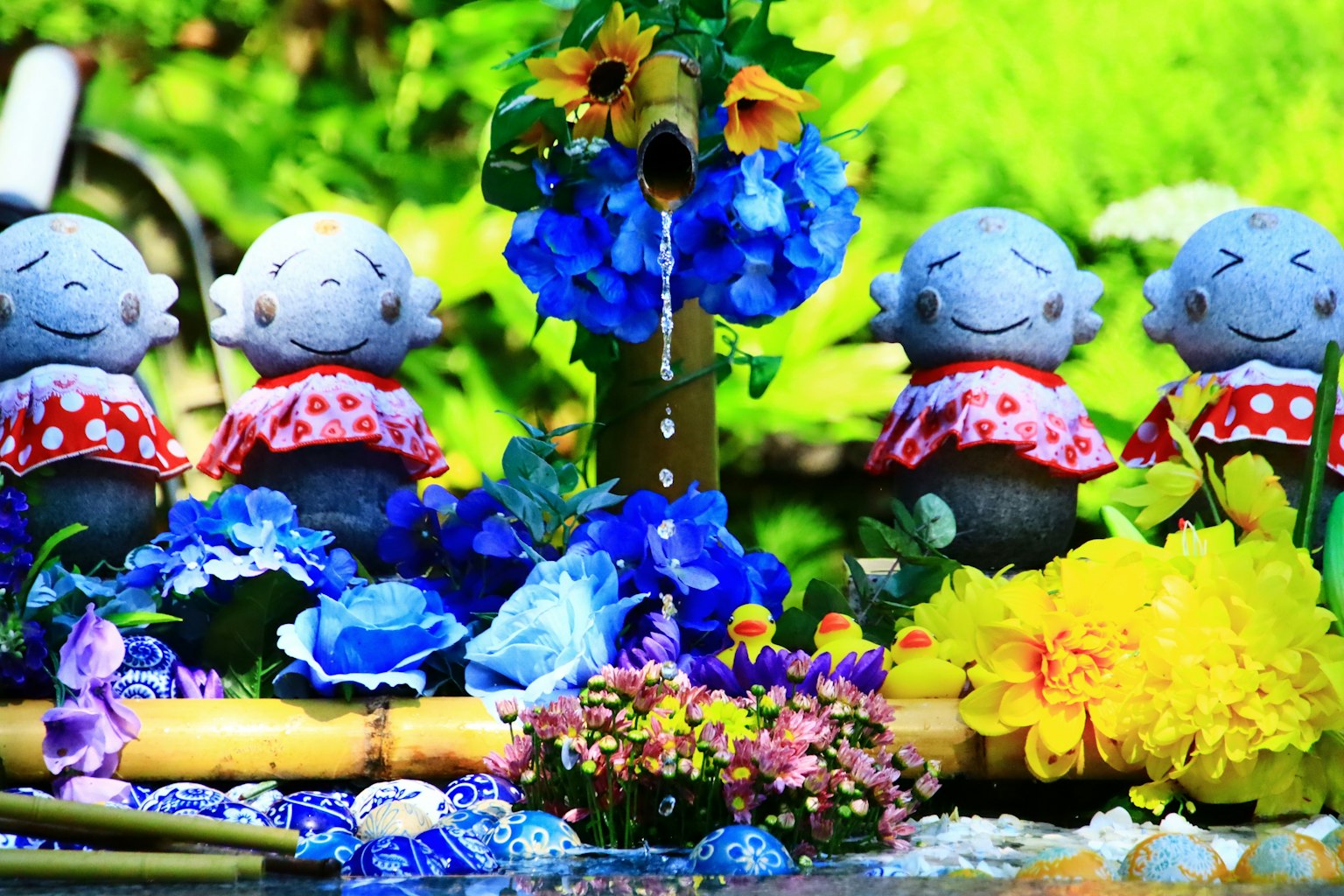 Fiori colorati e una fontana con figure in ceramica sorridenti nelle vicinanze