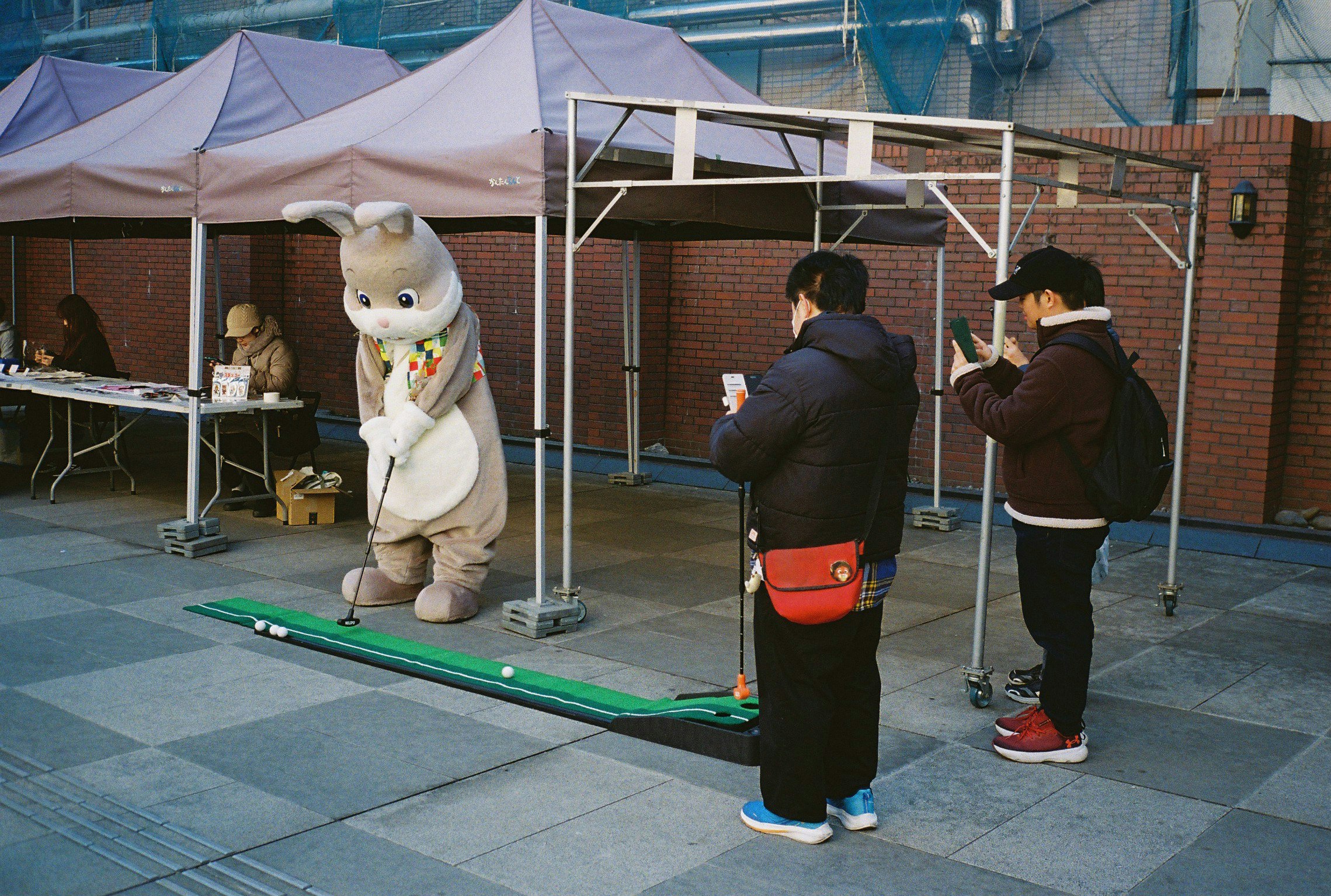 屋外のテント下で撮影用の着ぐるみと人がいるイベント会場