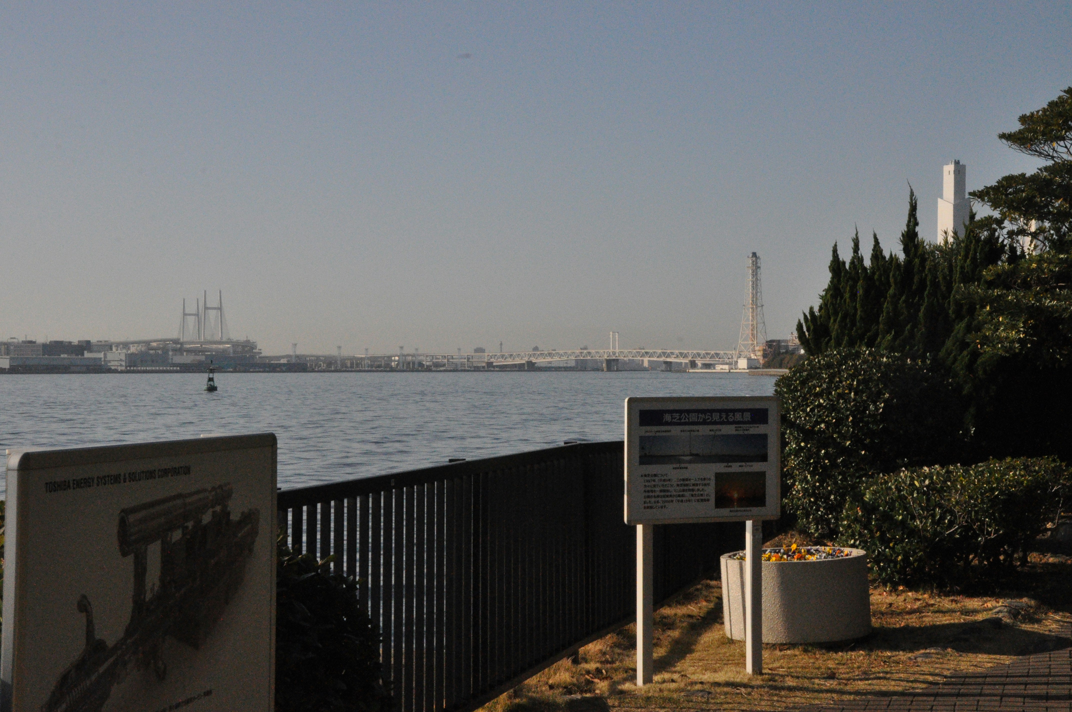 Paseo marítimo con carteles informativos y vista de un puente a lo lejos