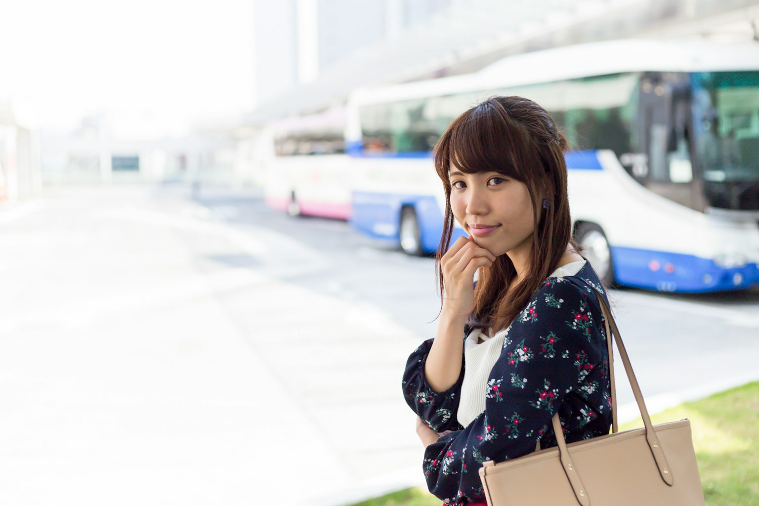 A woman pondering at a bus stop with buses parked in the background