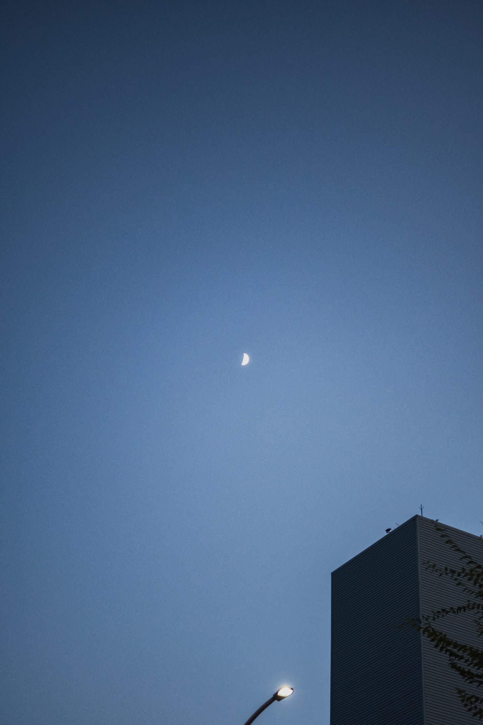 Moon in a blue sky with a building partially visible