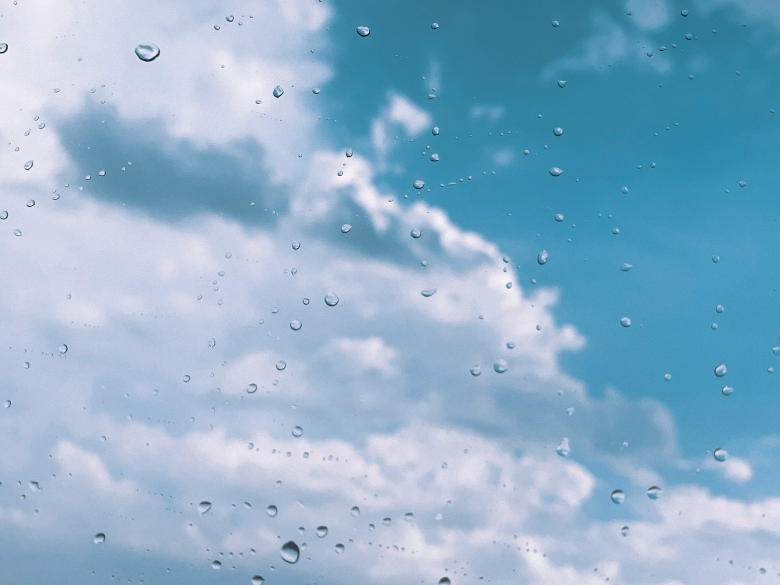 Gocce di pioggia su una finestra con cielo blu e nuvole sullo sfondo