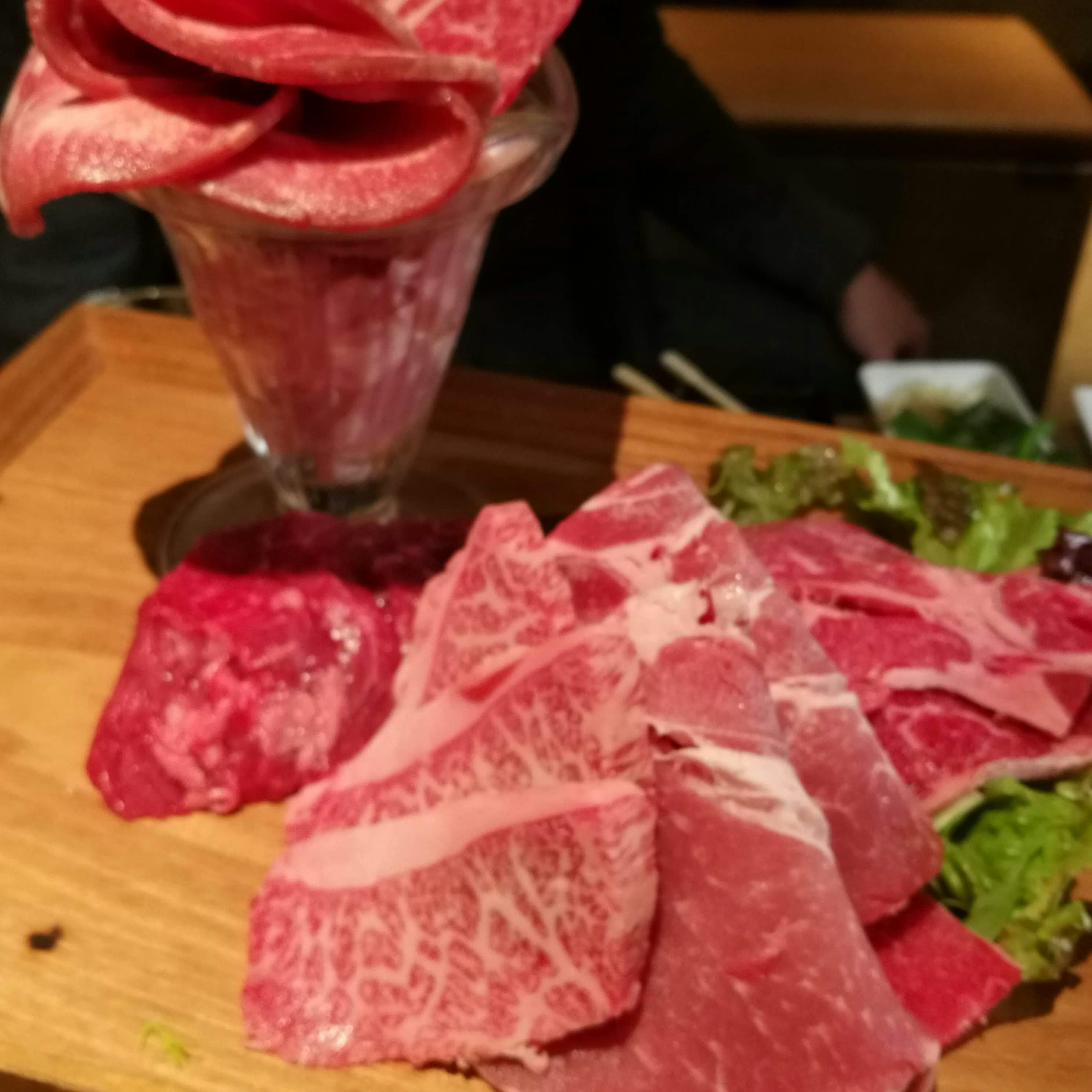 木のまな板に盛られた赤身の和牛とサラダの食卓