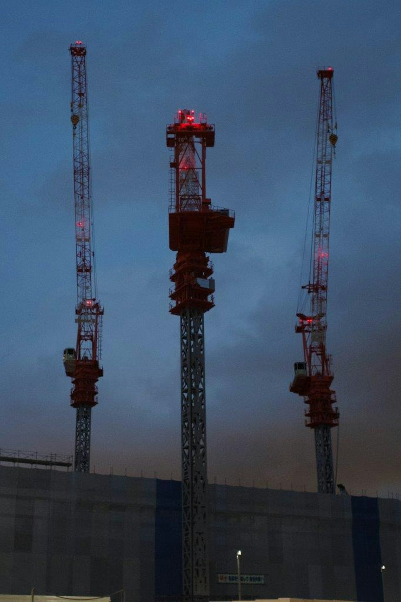 Three cranes with red lights blinking against the night sky