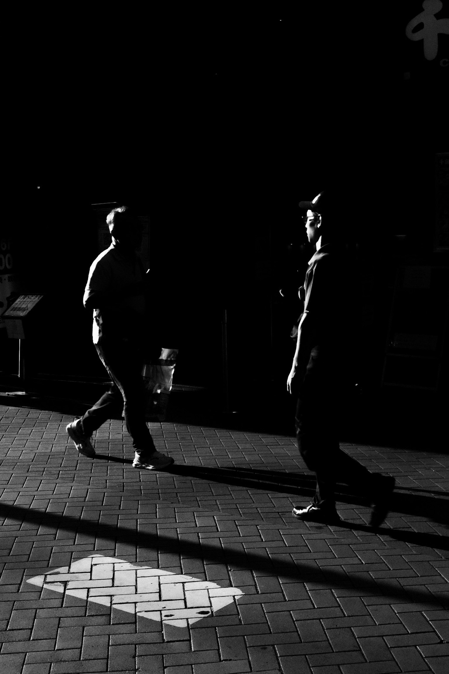 Two figures walking in a black and white scene with strong contrasts and shadows