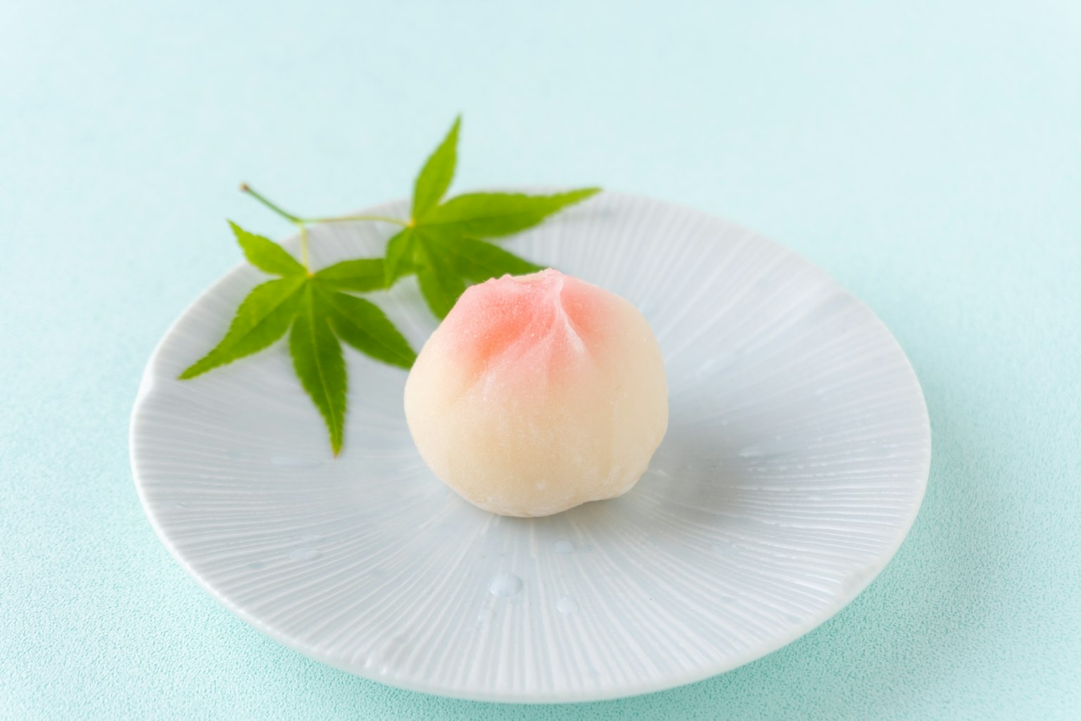 Pfirsichförmiger Wagashi auf einem weißen Teller mit grünen Blättern