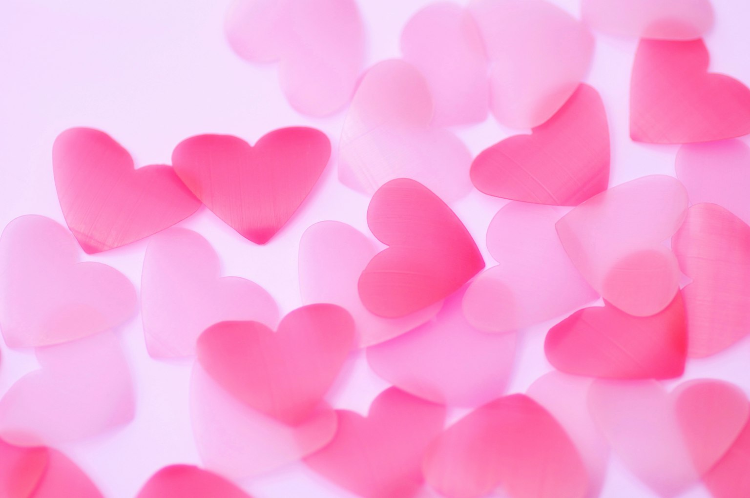 Dekorasi berbentuk hati berwarna pink yang tersebar di latar belakang terang