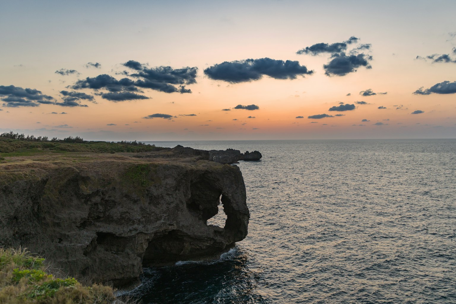 Vue du coucher de soleil sur une falaise surplombant la mer avec de grandes formations rocheuses et des nuages