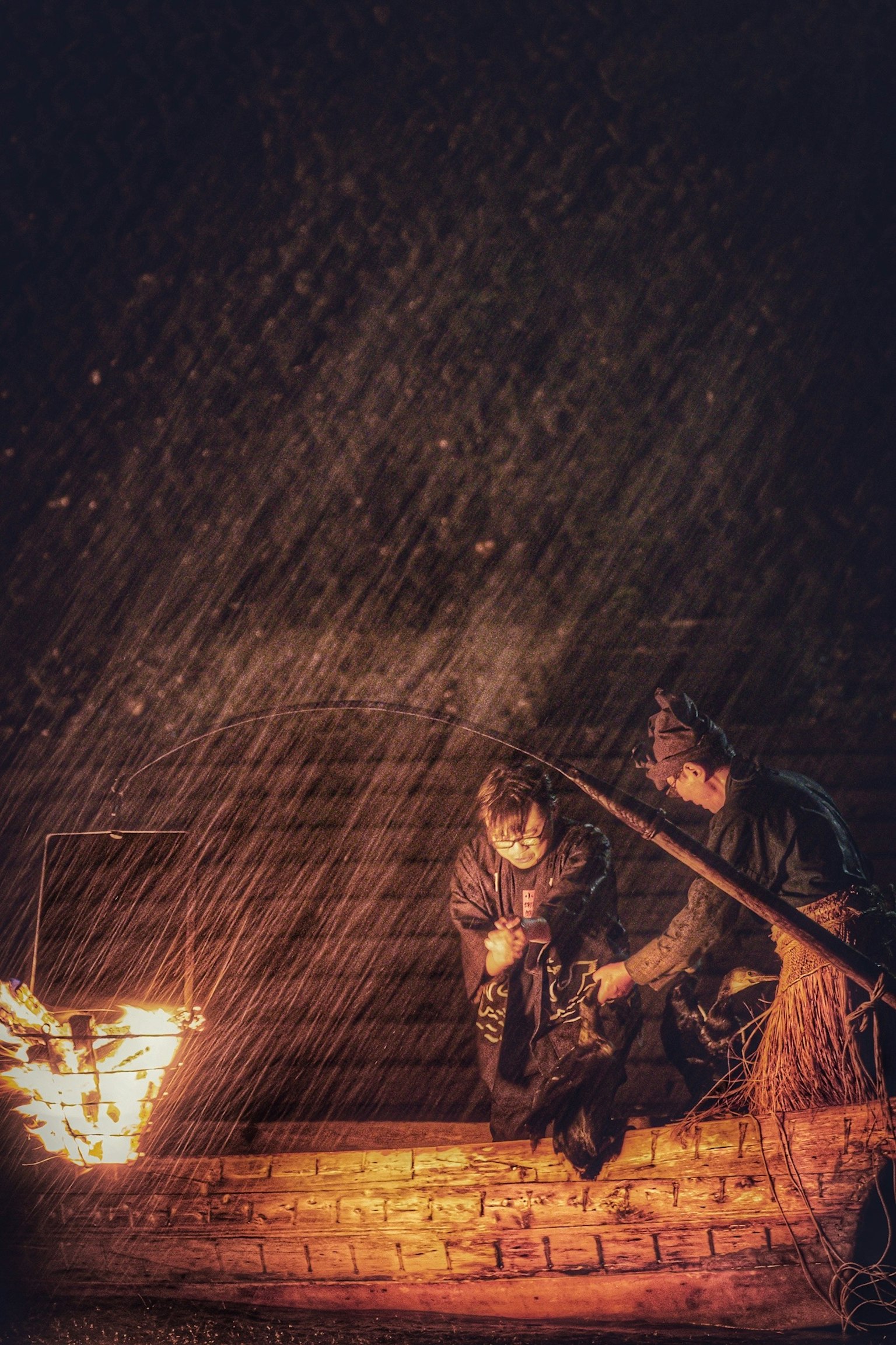 Two fishermen gathered around a fire on a dark water surface