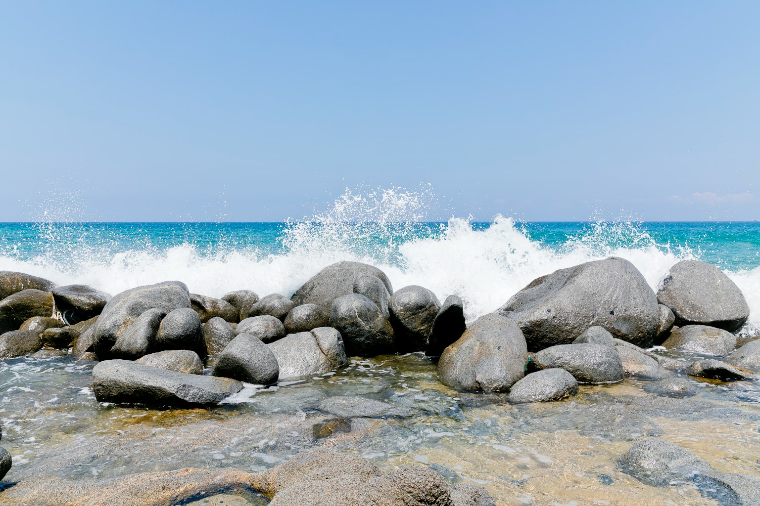 Scène côtière avec des vagues frappant un rivage rocheux sous un ciel bleu clair