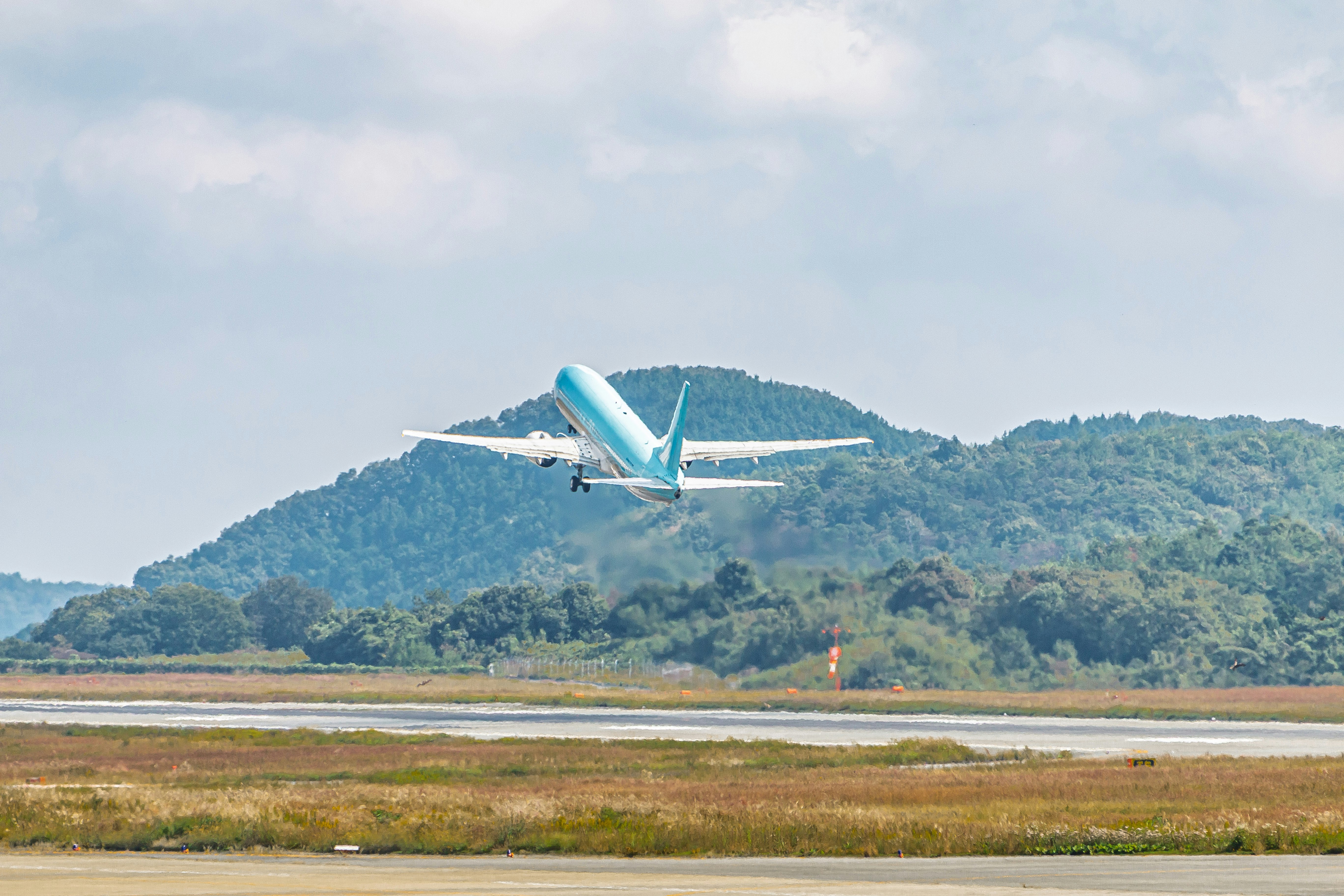 滑走路を飛び立つ旅客機と緑の丘の風景