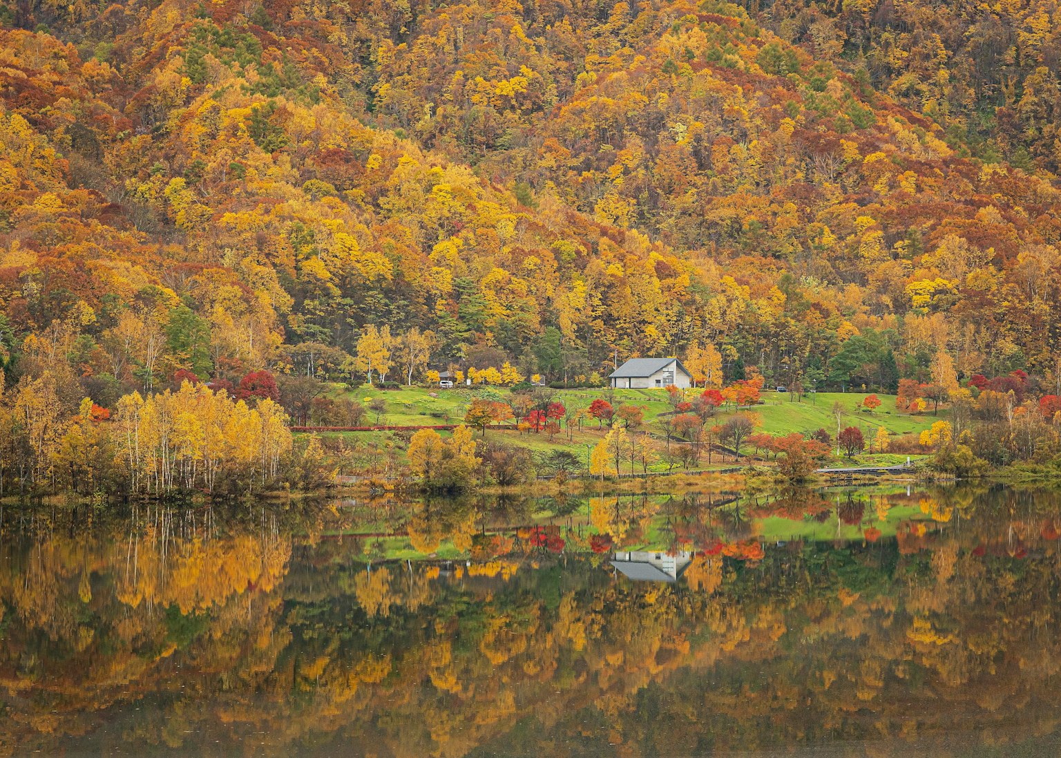 Scenic autumn landscape with colorful foliage covering hills near a tranquil lake with a house