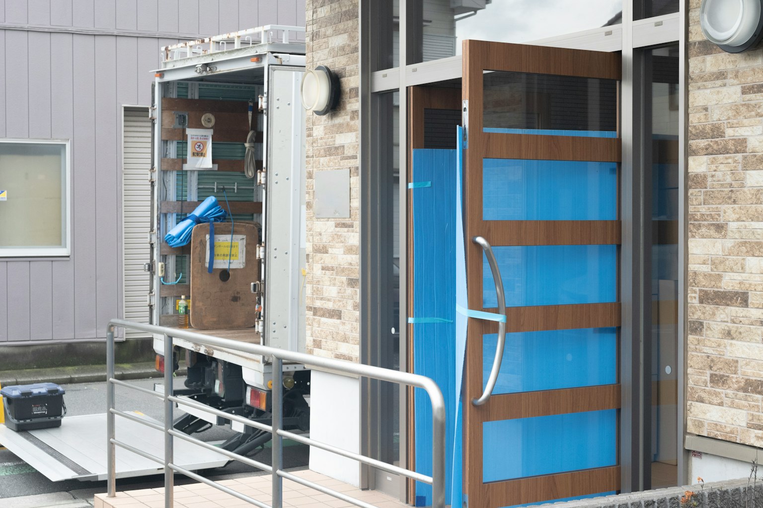 Entrada de un edificio con una puerta azul y un camión cargado de paquetes