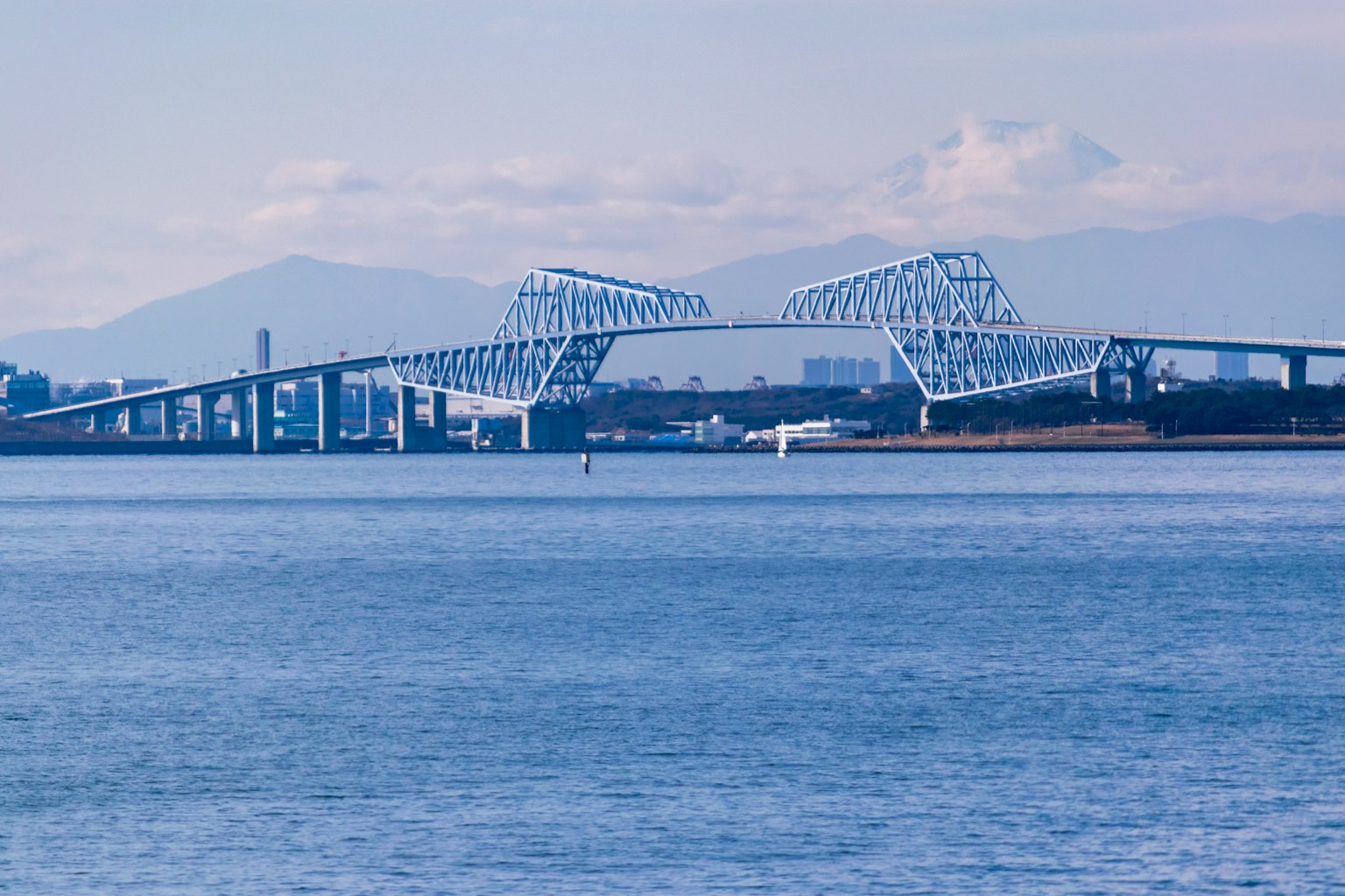 Unique design bridge reflected on blue water with mountains in the background