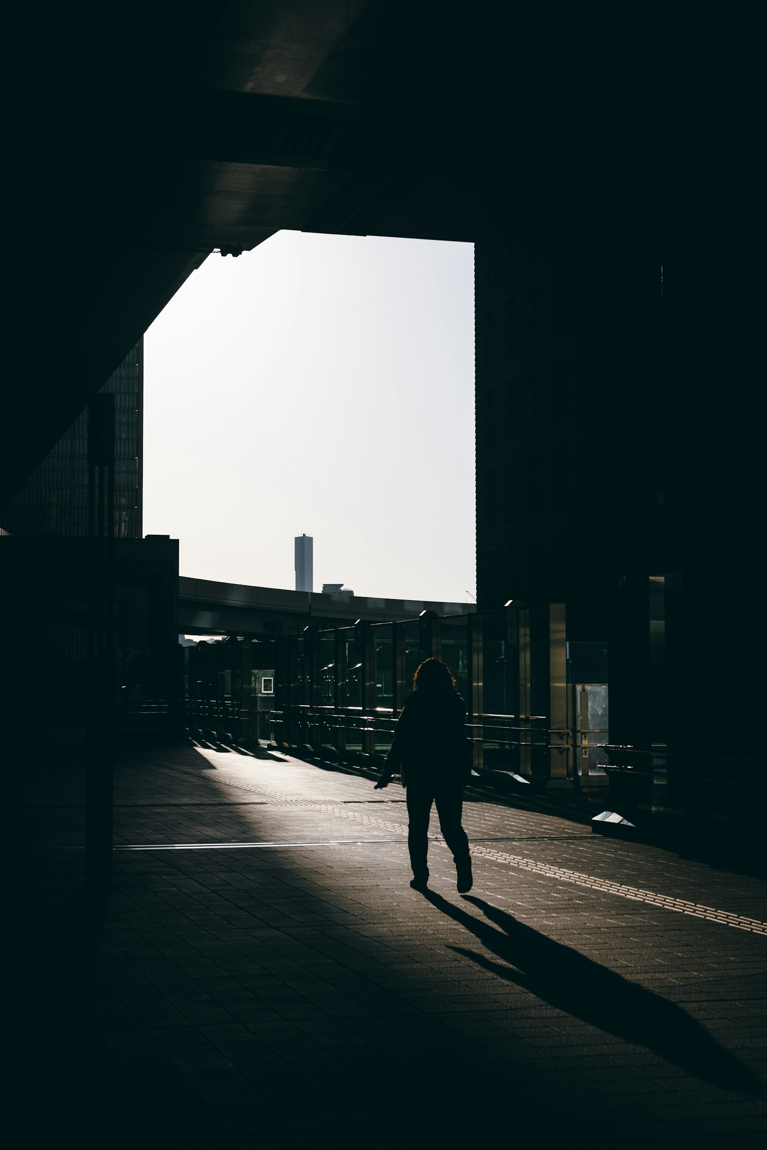 Silhouette d'une personne marchant dans un passage urbain sombre ciel lumineux en arrière-plan
