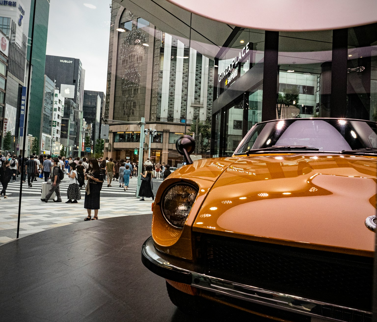 Classic orange car displayed in a shopping district with modern buildings