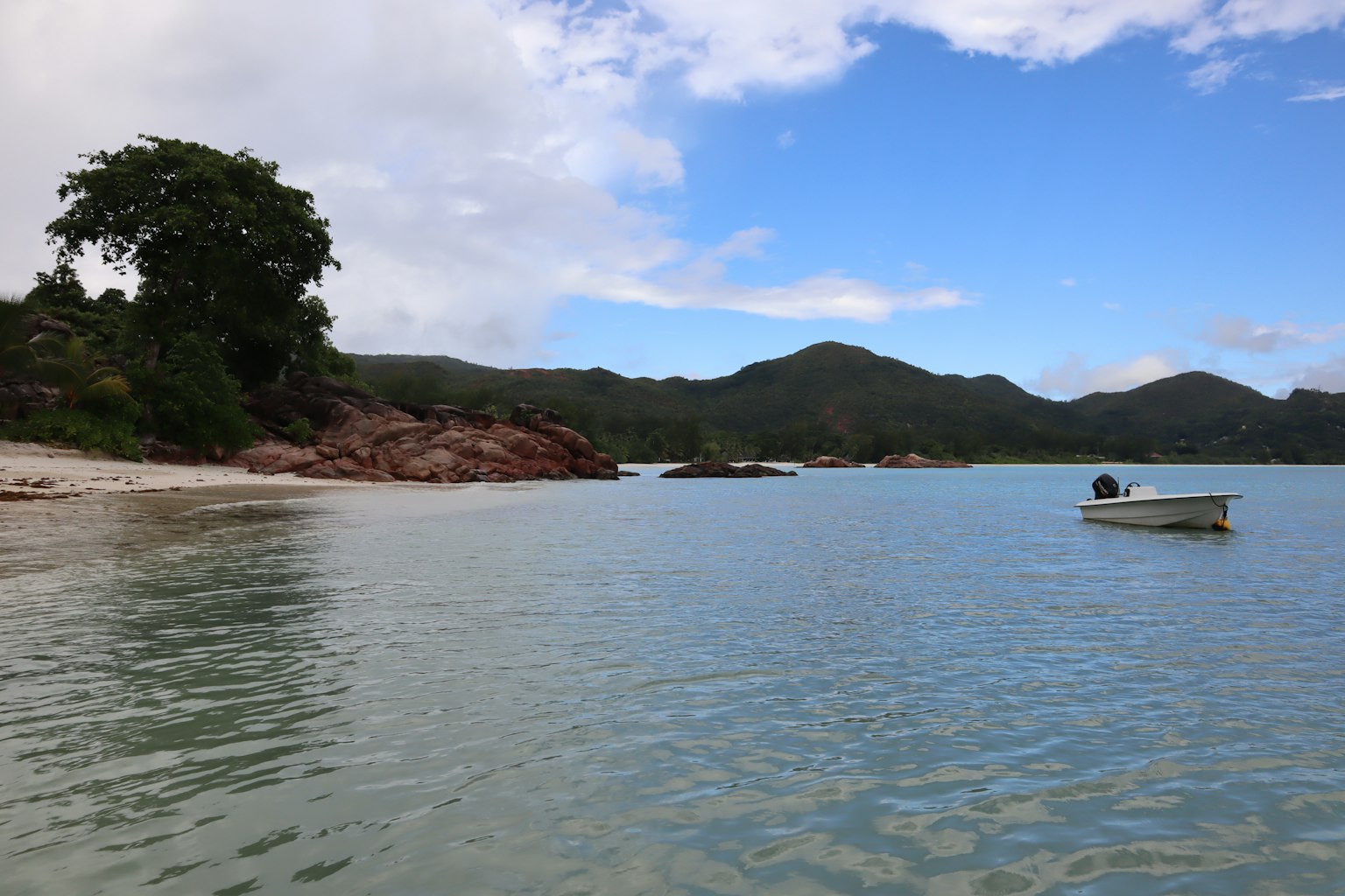 Un petit bateau flottant sur des eaux calmes sous un ciel bleu avec des nuages épars et des collines verdoyantes en arrière-plan